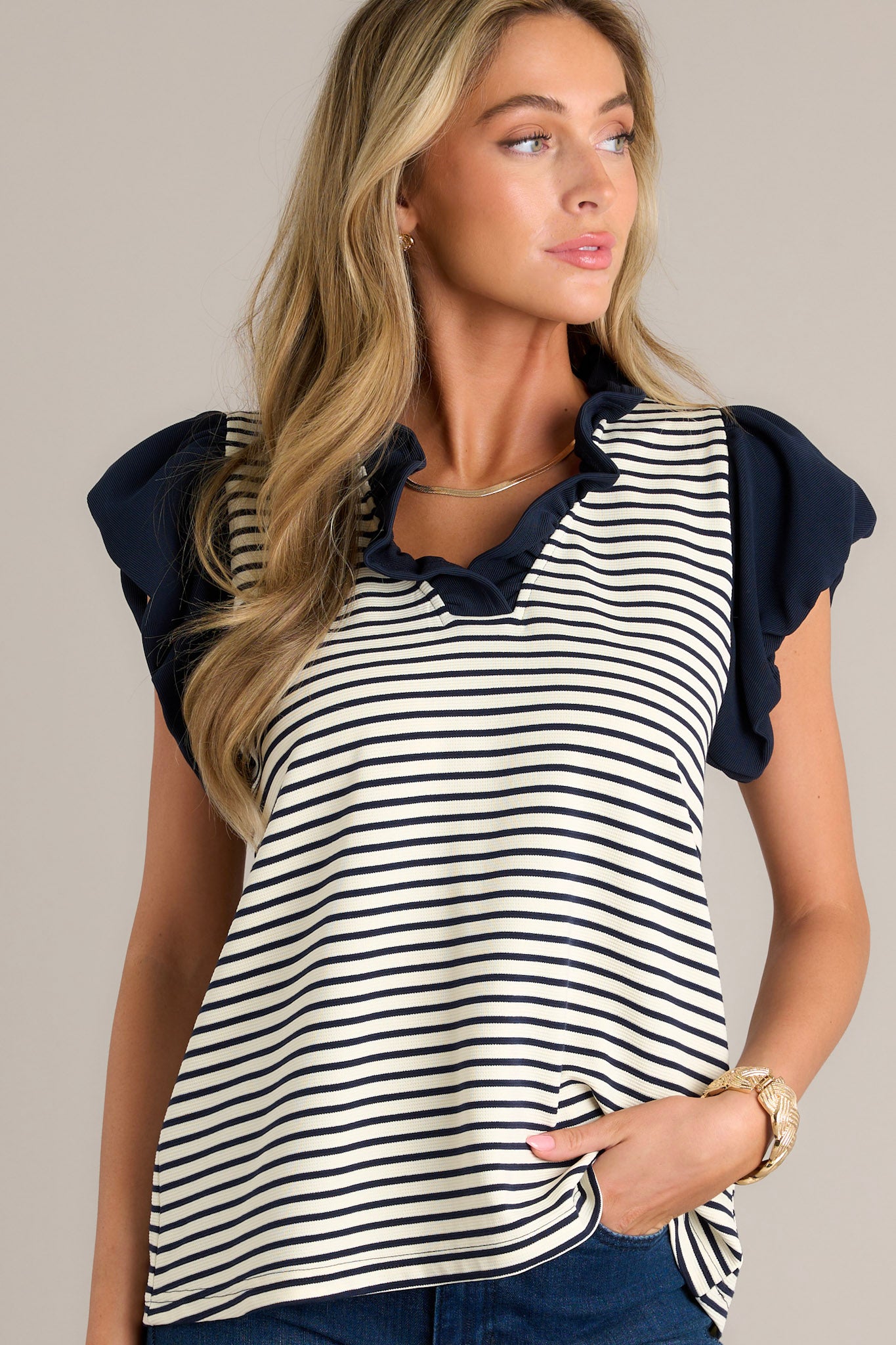 This beige stripe blouse features a navy ruffle v-neckline, navy and beige horizontal stripes, and slightly cuffed short sleeves.