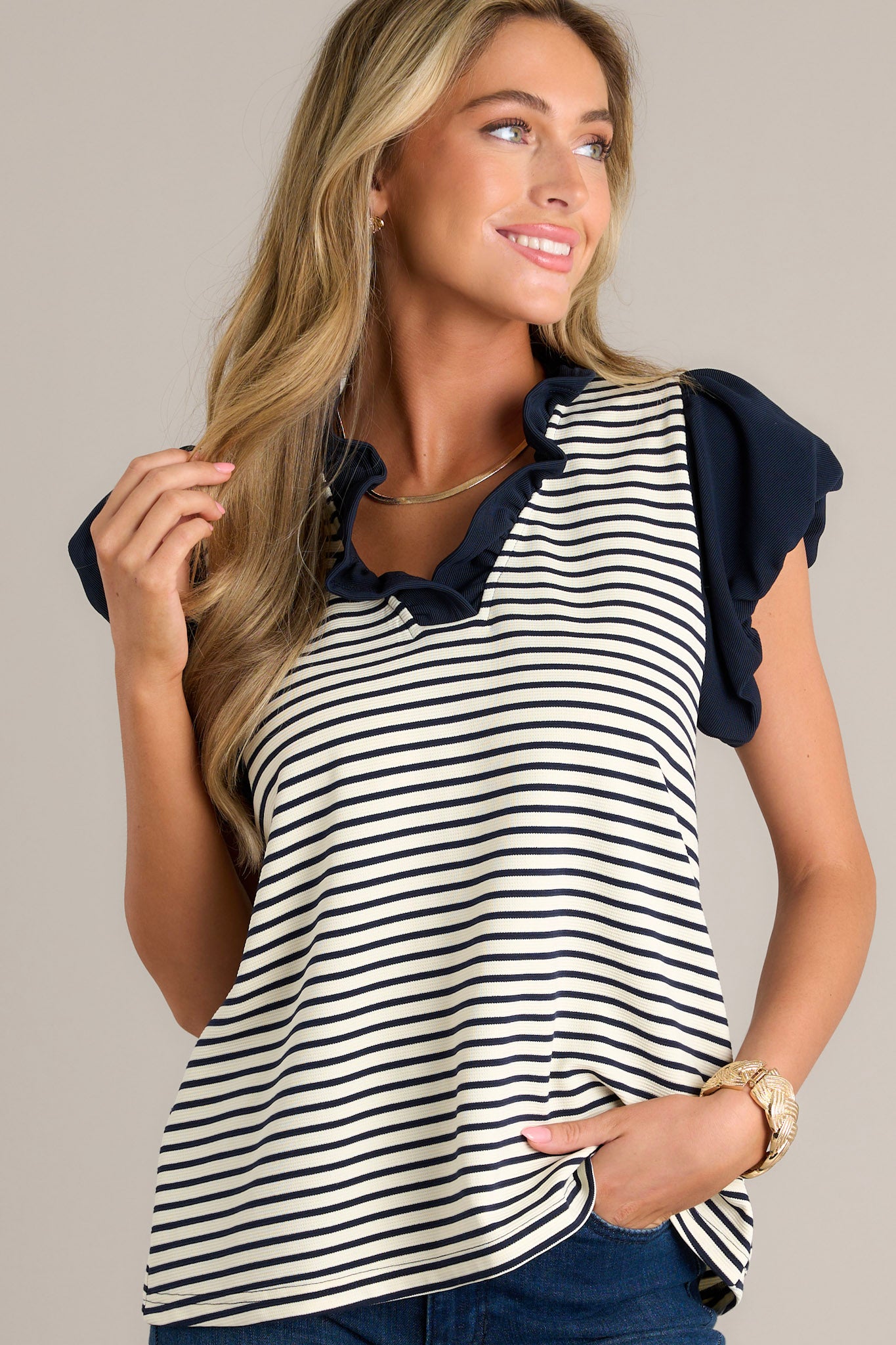 Front view of a beige stripe blouse featuring a navy ruffle v-neckline, navy and beige horizontal stripes, and slightly cuffed short sleeves.