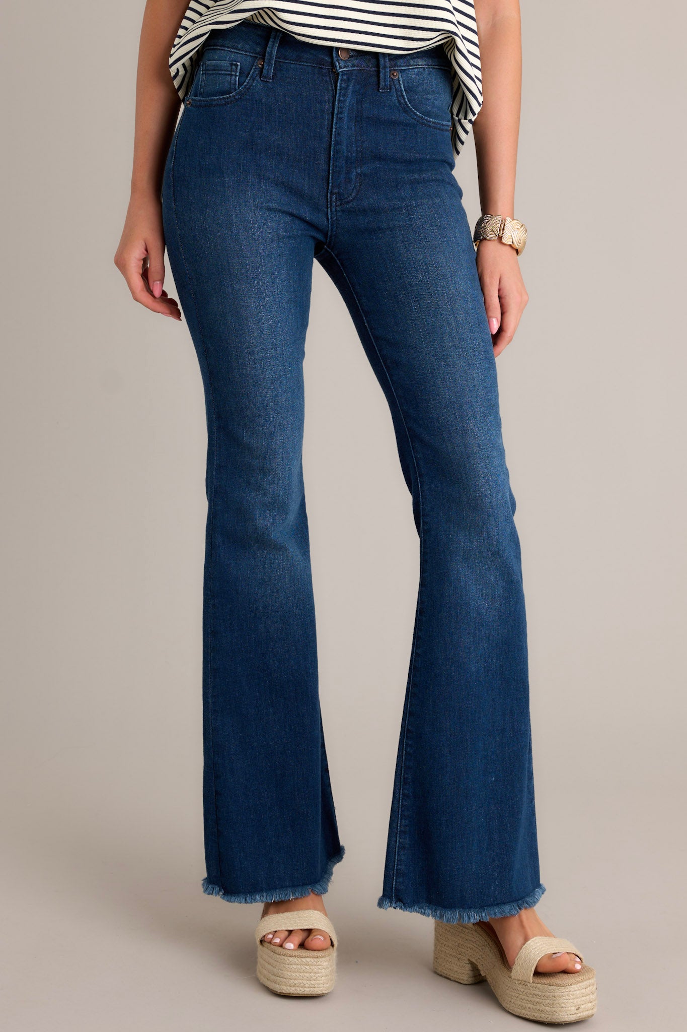 Front view of these jeans that feature a high waist, classic button zipper closure, five functional pockets, flared leg, and a raw hemline.