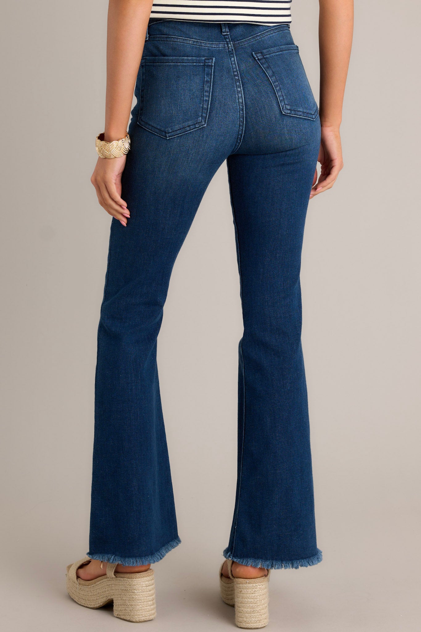 Back view of these jeans that feature a high waist, classic button zipper closure, five functional pockets, flared leg, and a raw hemline.