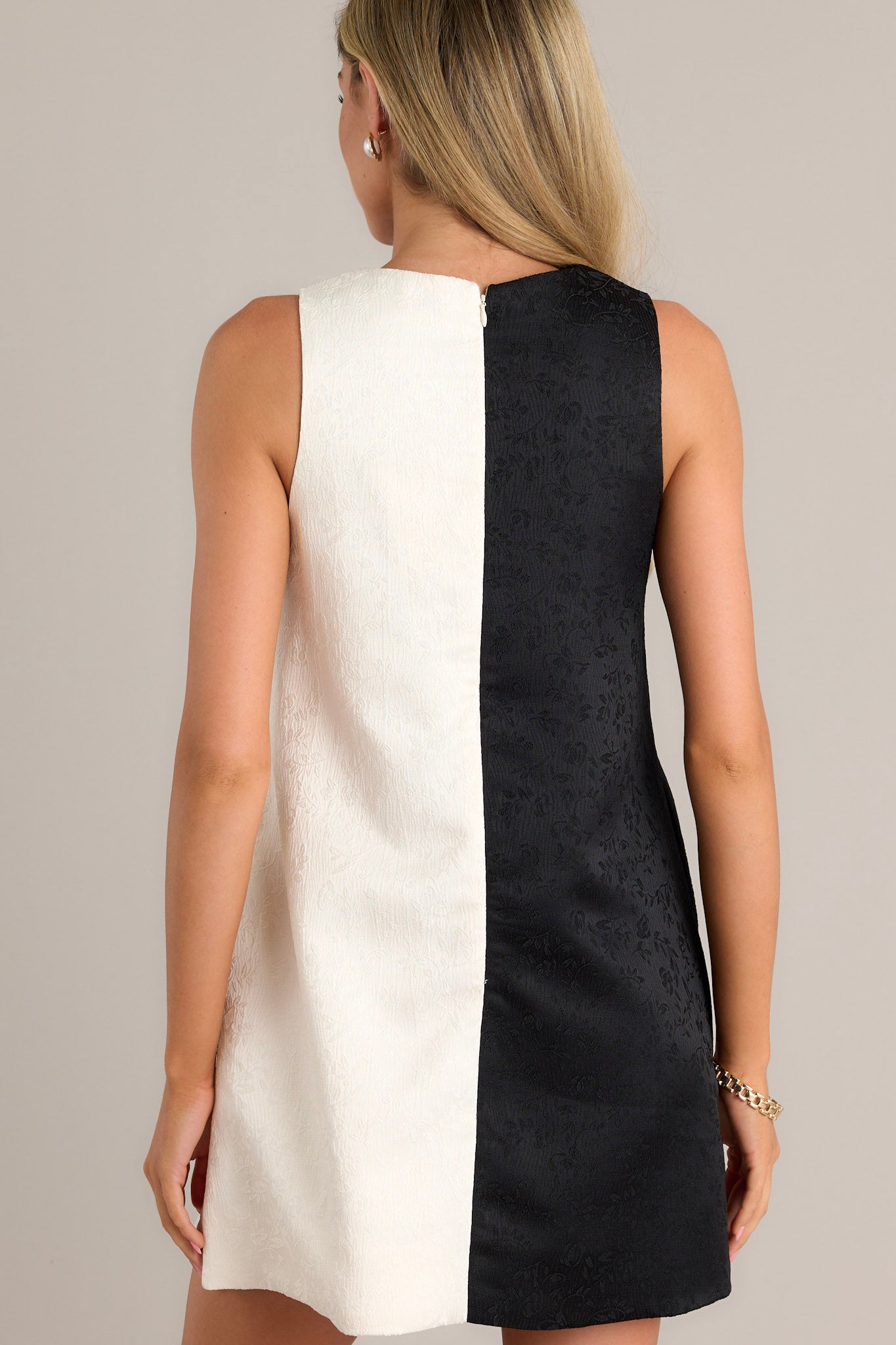 Back view of a black mini dress highlighting the overall fit, color block design, and sleeveless design.