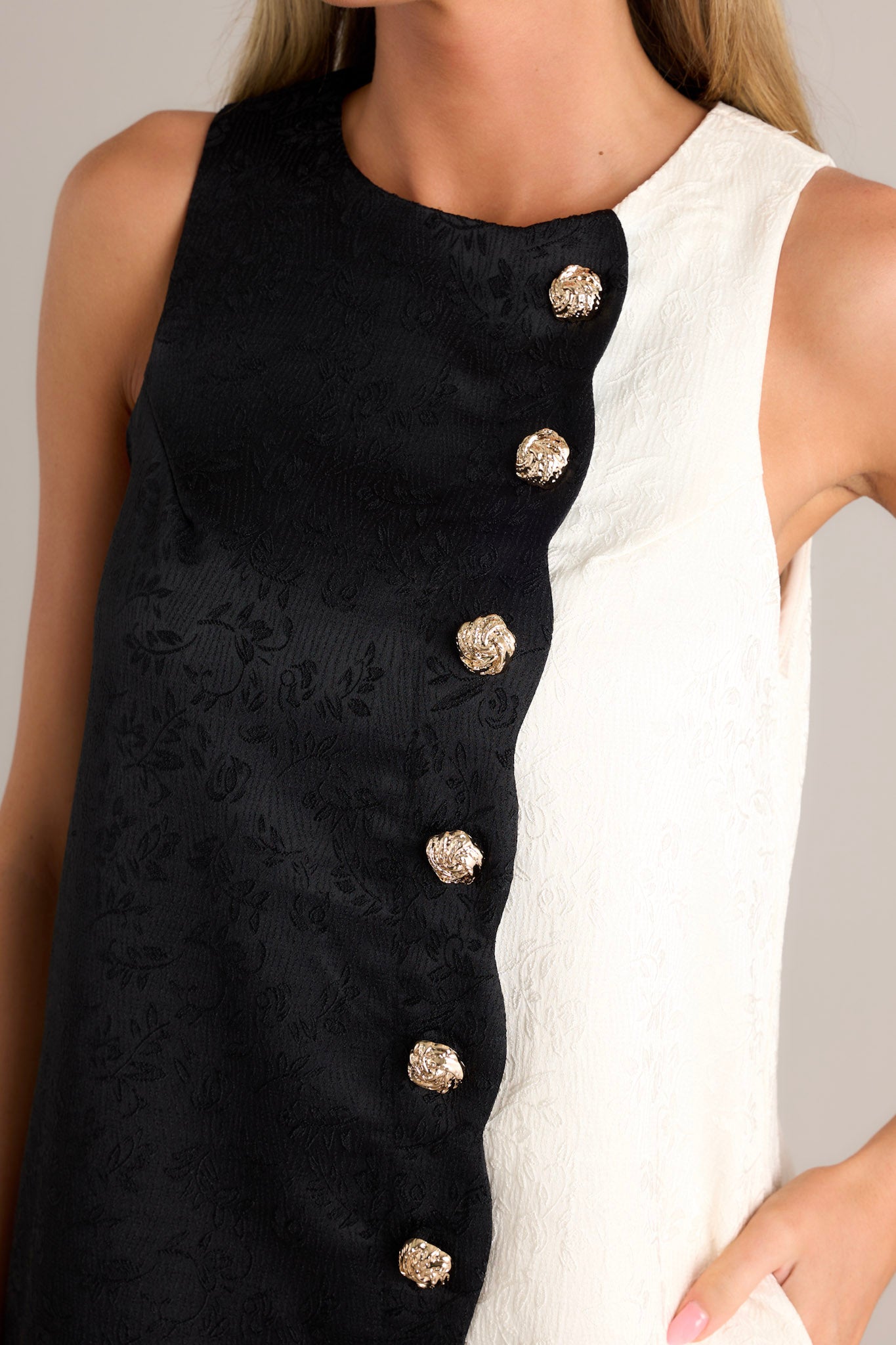 Close-up of the black mini dress showing the crew neckline, faux textured buttons, and color block design.