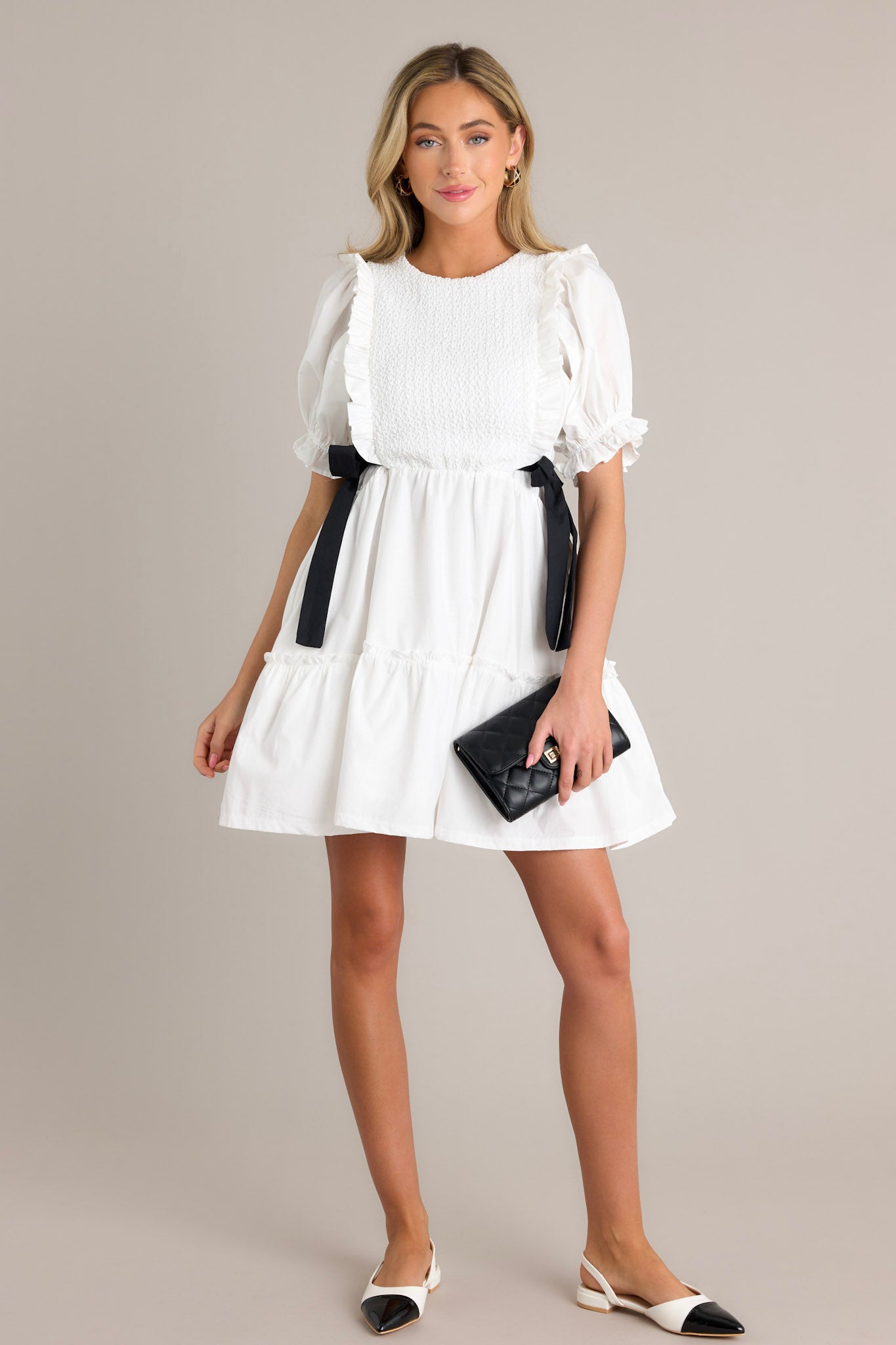 This ivory mini dress features a smocked bodice design, self tie waist bows, a tiered design, a discrete back zipper, and cuffed puffer sleeves.