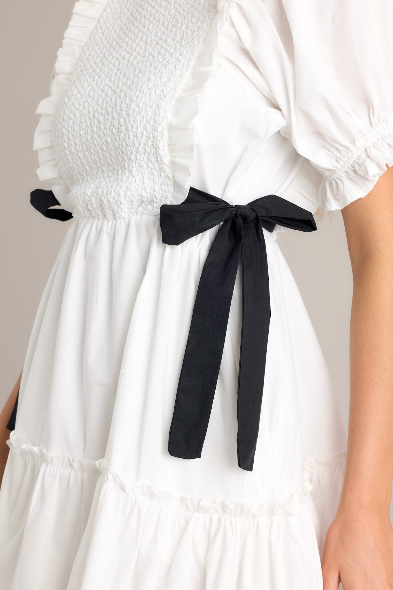 Close-up of the ivory mini dress showing the smocked bodice design, self-tie waist bows, and cuffed puffer sleeves.