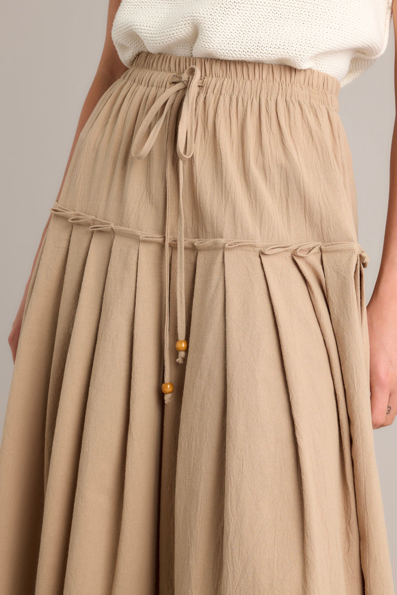 Close-up of the beige maxi skirt showing the self-tie drawstring, elastic waistband, and subtle pleats.