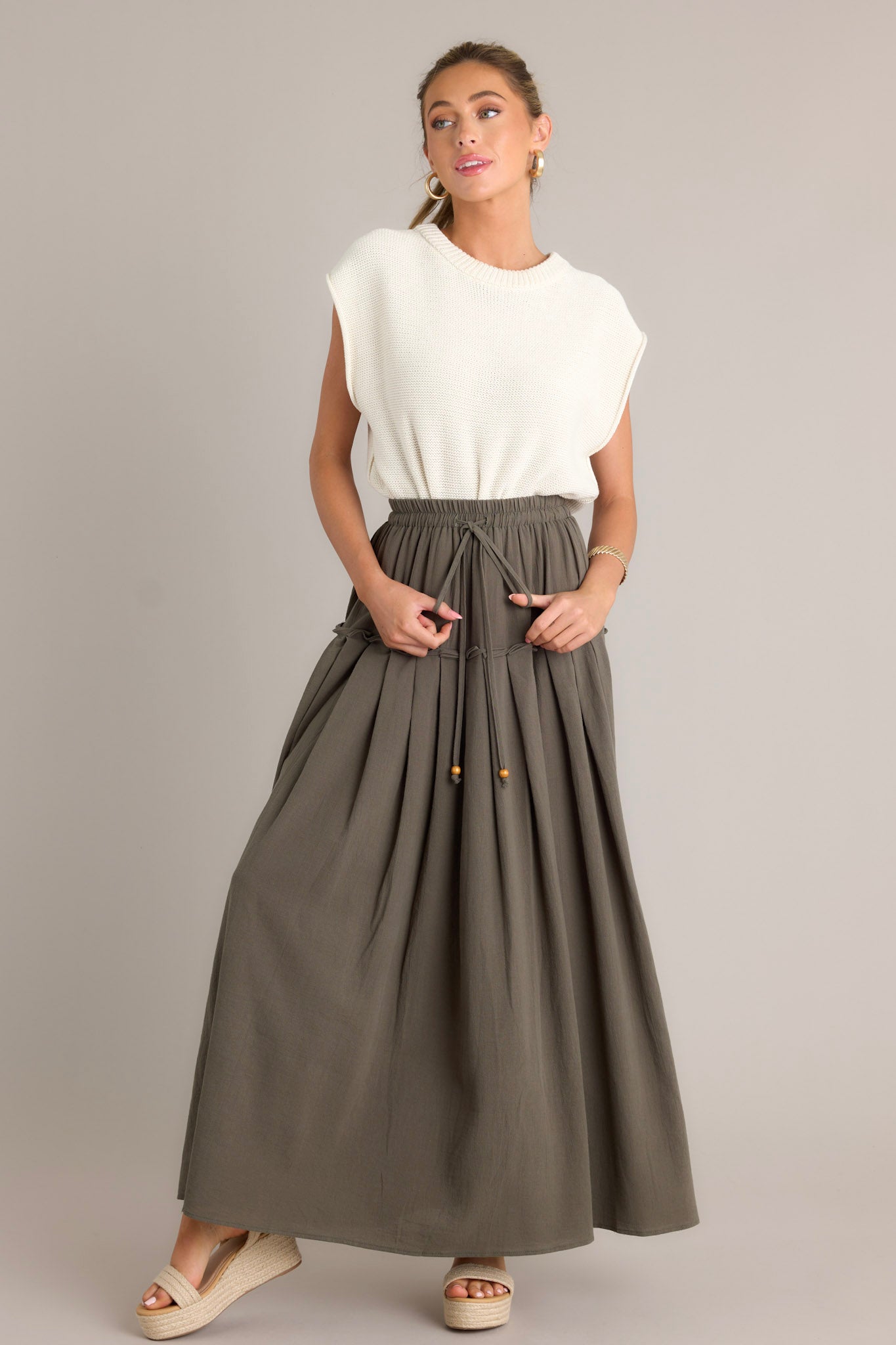 This olive maxi skirt features a high waisted design, an elastic waistband, a self-tie drawstring, a single tier, subtle pleats, and a flowing silhouette.