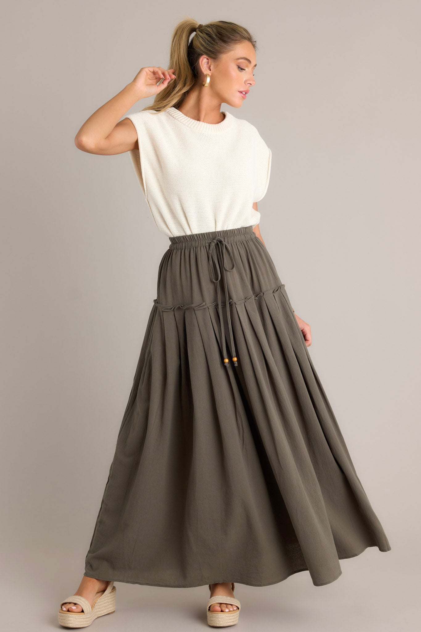 Action shot of an olive maxi skirt displaying the fit and movement, highlighting the high waisted design, elastic waistband, self-tie drawstring, single tier, subtle pleats, and flowing silhouette.