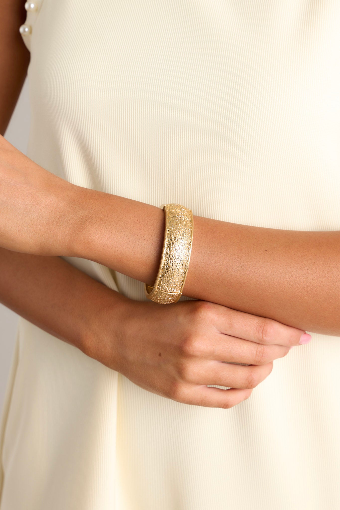 This gold bracelet features a heavily textured material, and elastic bands underneath to accommodate stretch.
