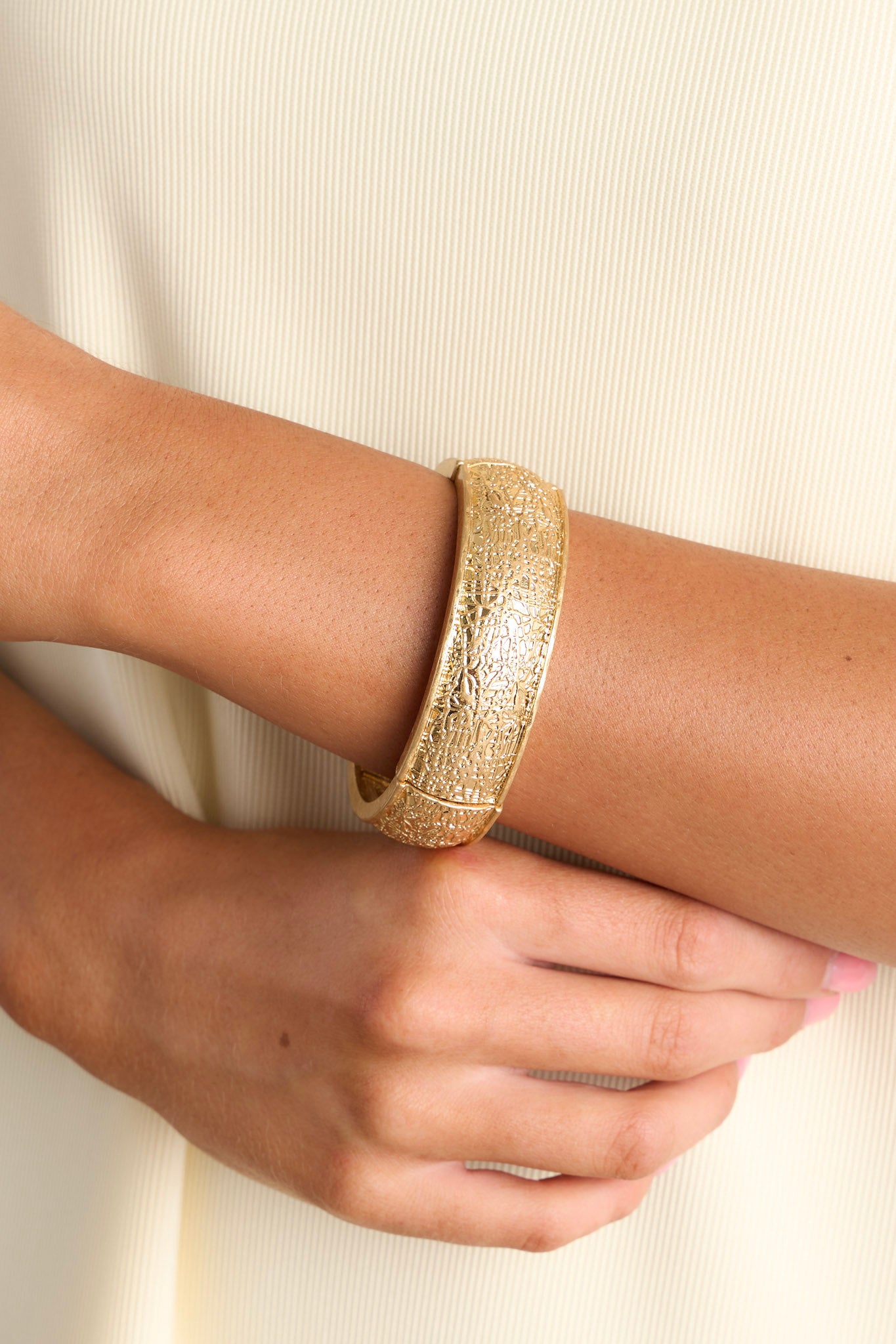 Close-up view of this gold bracelet that features a heavily textured material, and elastic bands underneath to accommodate stretch.