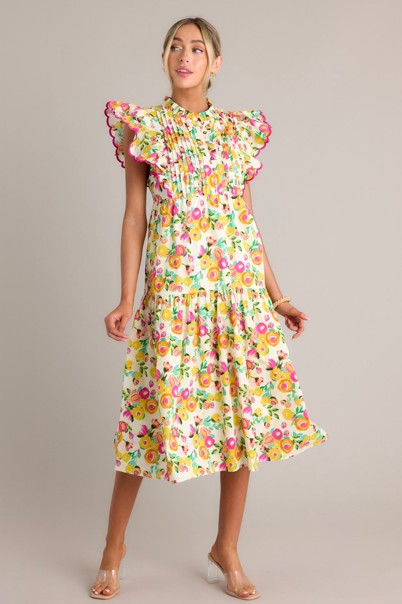 This yellow floral midi dress features a high ruffled neckline, a functional button front bodice, a pleated chest, functional hip pockets, a single tier, and short flutter sleeves.