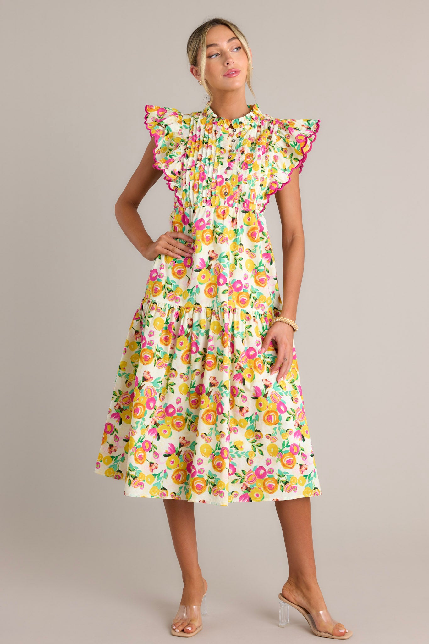 Full length view of a yellow floral midi dress with a high ruffled neckline, a functional button front bodice, a pleated chest, functional hip pockets, a single tier, and short flutter sleeves