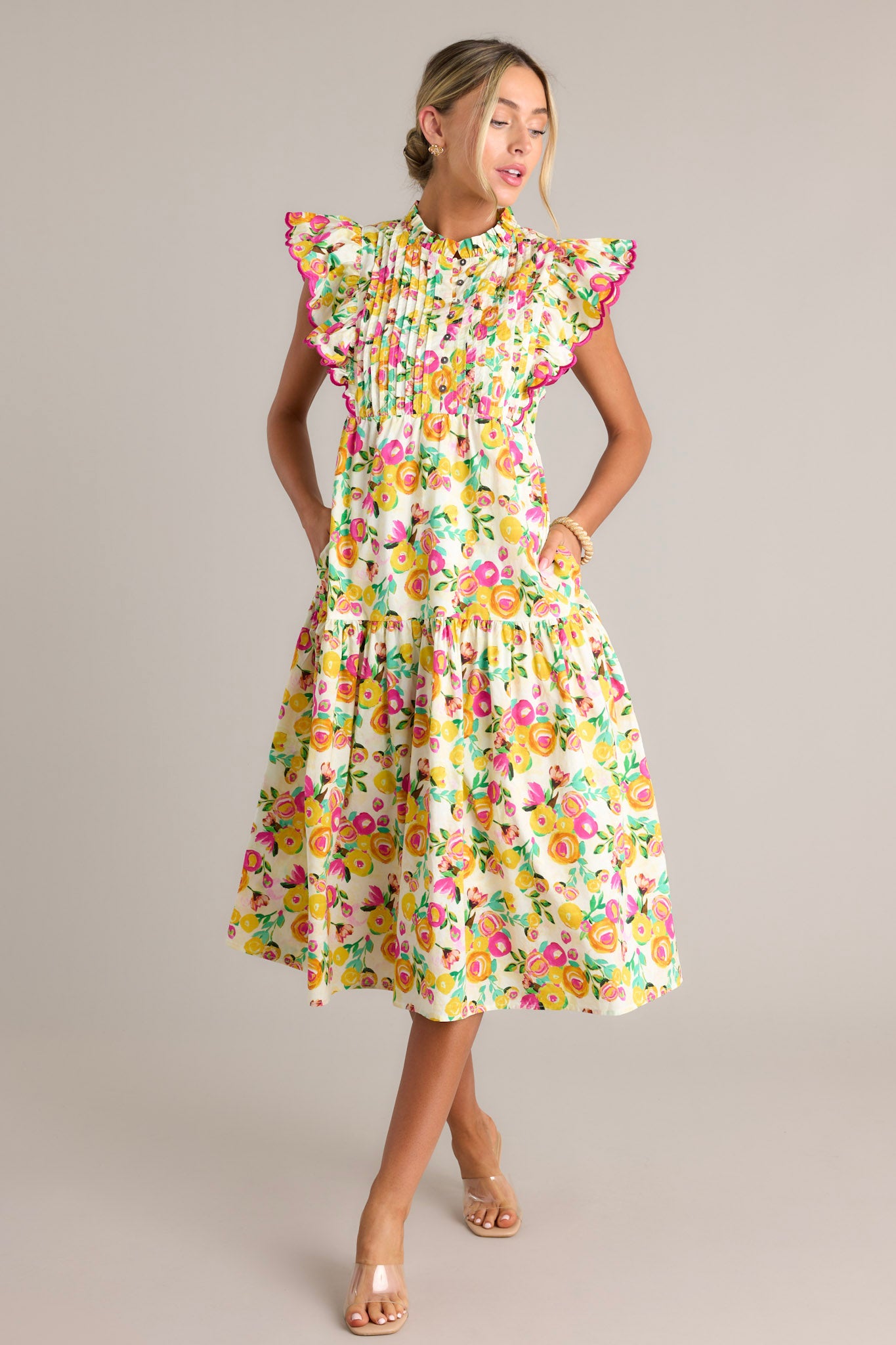 Action shot of a yellow floral midi dress displaying the fit and movement, highlighting the high ruffled neckline, functional button front bodice, pleated chest, functional hip pockets, single tier, and short flutter sleeves.