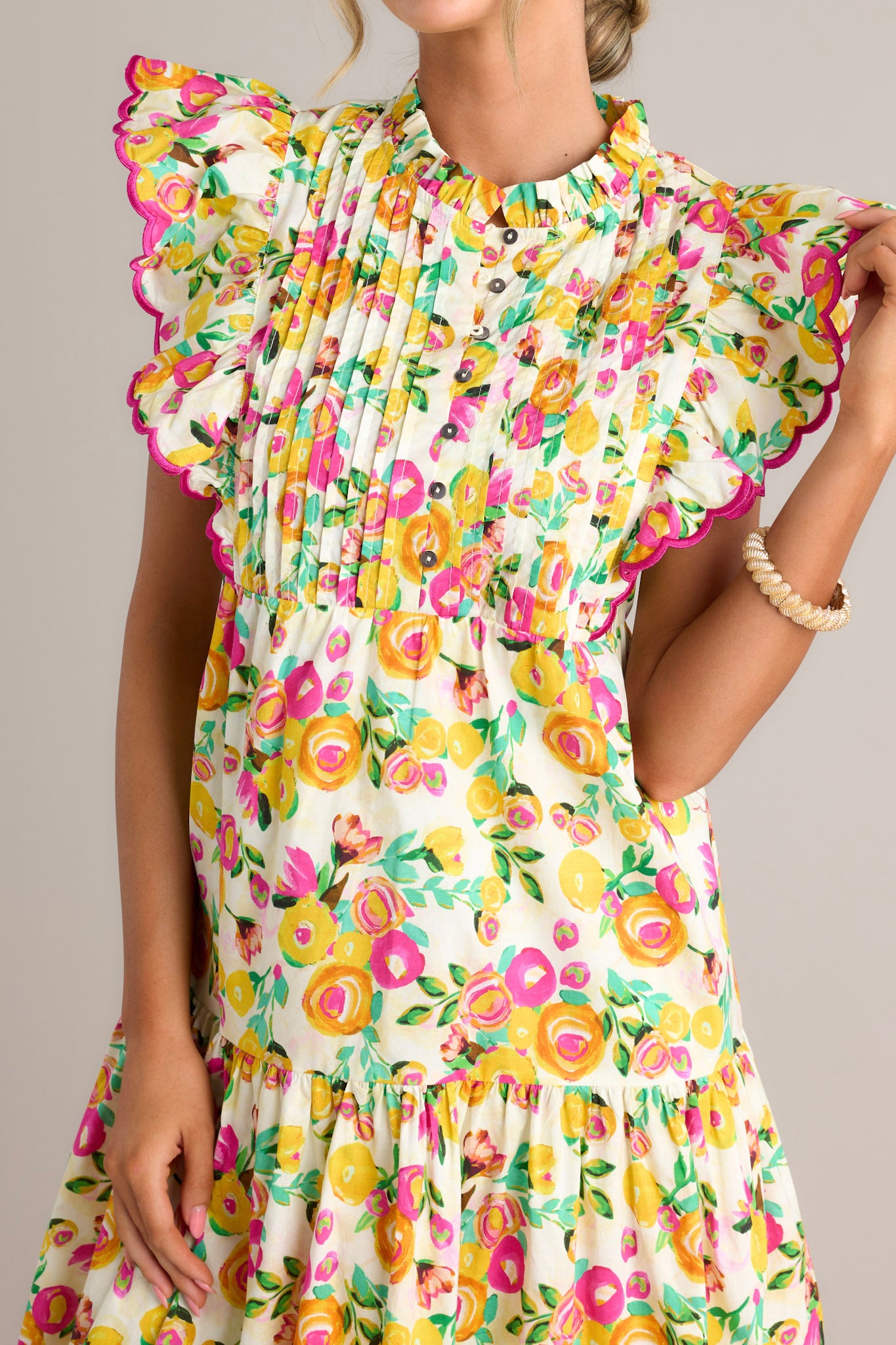 Close-up of the yellow floral midi dress showing the high ruffled neckline, functional button front bodice, and pleated chest.