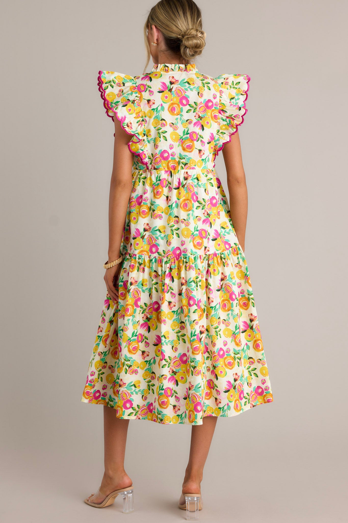 Back view of a yellow floral midi dress highlighting the high ruffled neckline, single tier, and overall fit.