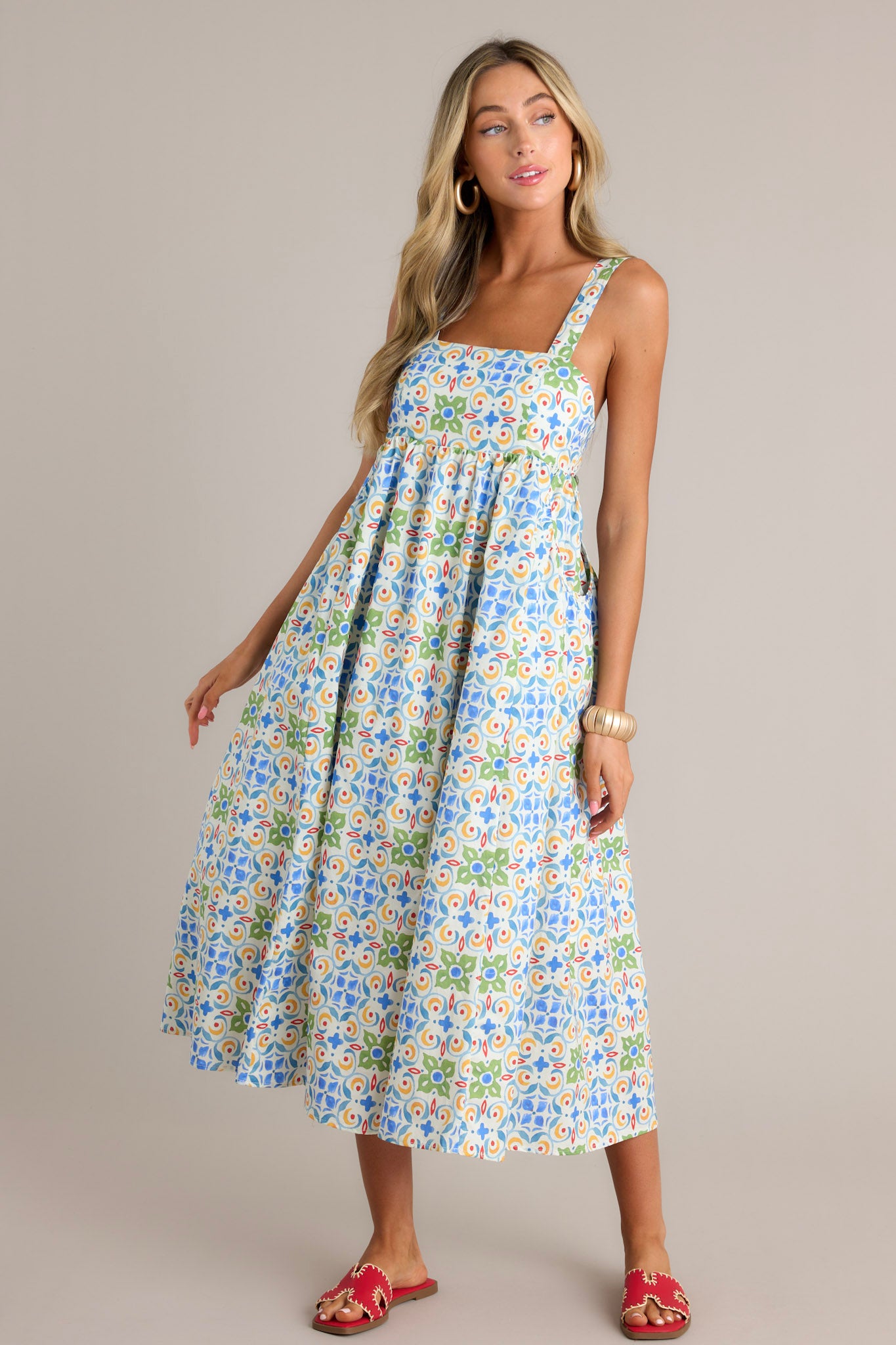 Front angled view of a white midi dress featuring a square neckline, self-tie adjustable straps, a colorful pattern, functional hip pockets, and a flowing silhouette