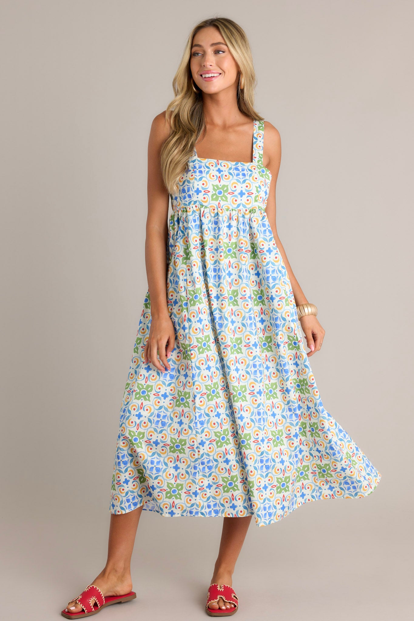 Full length view of a white midi dress with a square neckline, self-tie adjustable straps, a colorful pattern, functional hip pockets, and a flowing silhouette