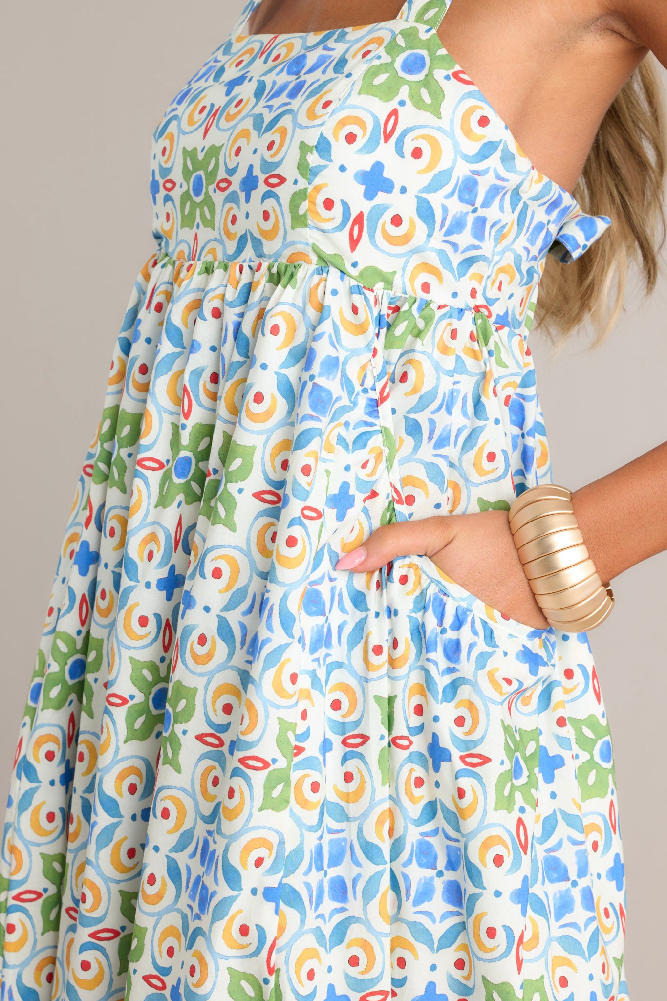 Side view of a white midi dress showcasing the square neckline, self-tie adjustable straps, colorful pattern, functional hip pockets, and flowing silhouette.