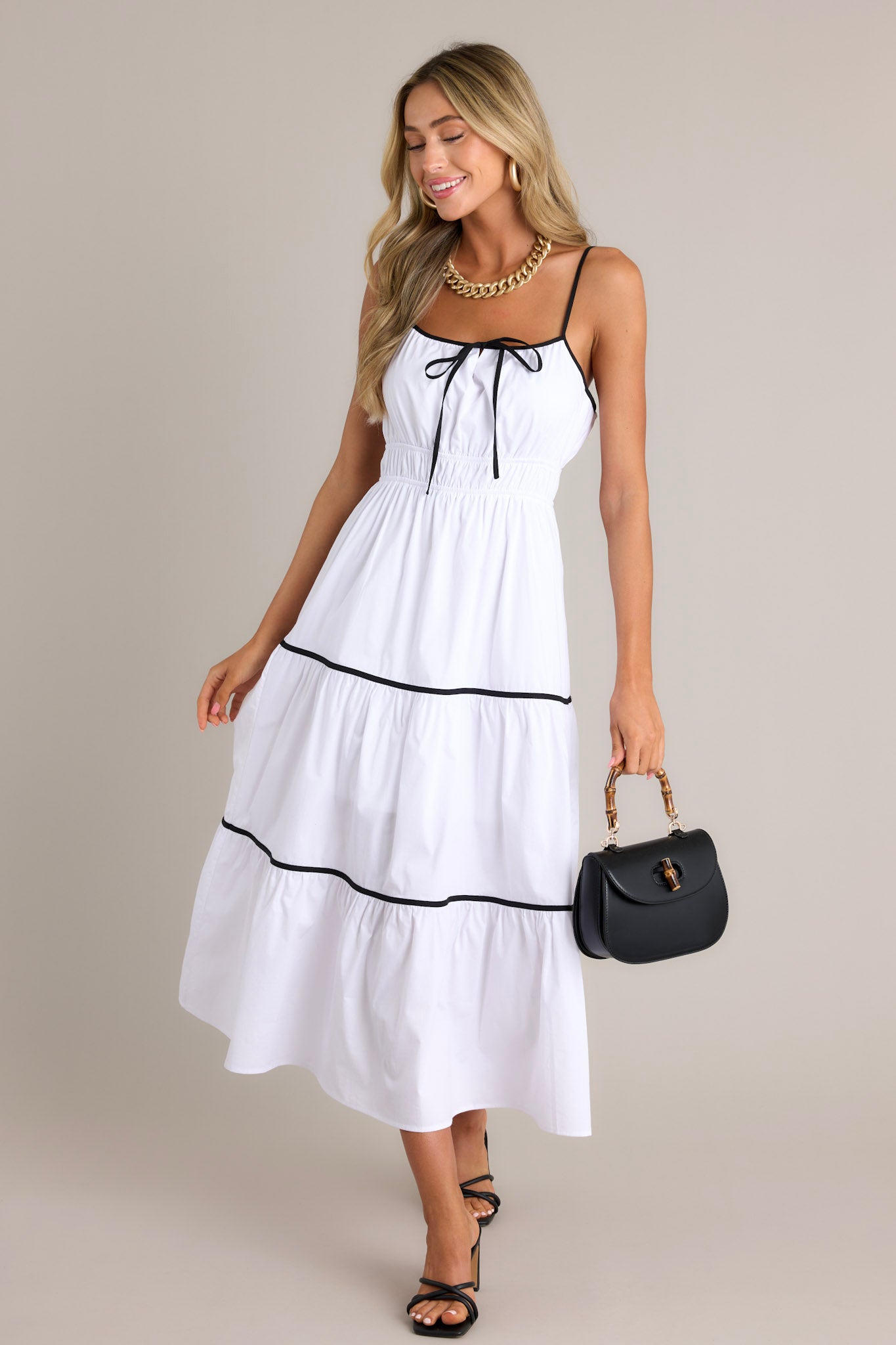 Action shot of a white midi dress displaying the fit and movement, highlighting the square neckline, thin adjustable straps, self-tie bust feature, elastic waist, contrasting tiers, and flowing silhouette.