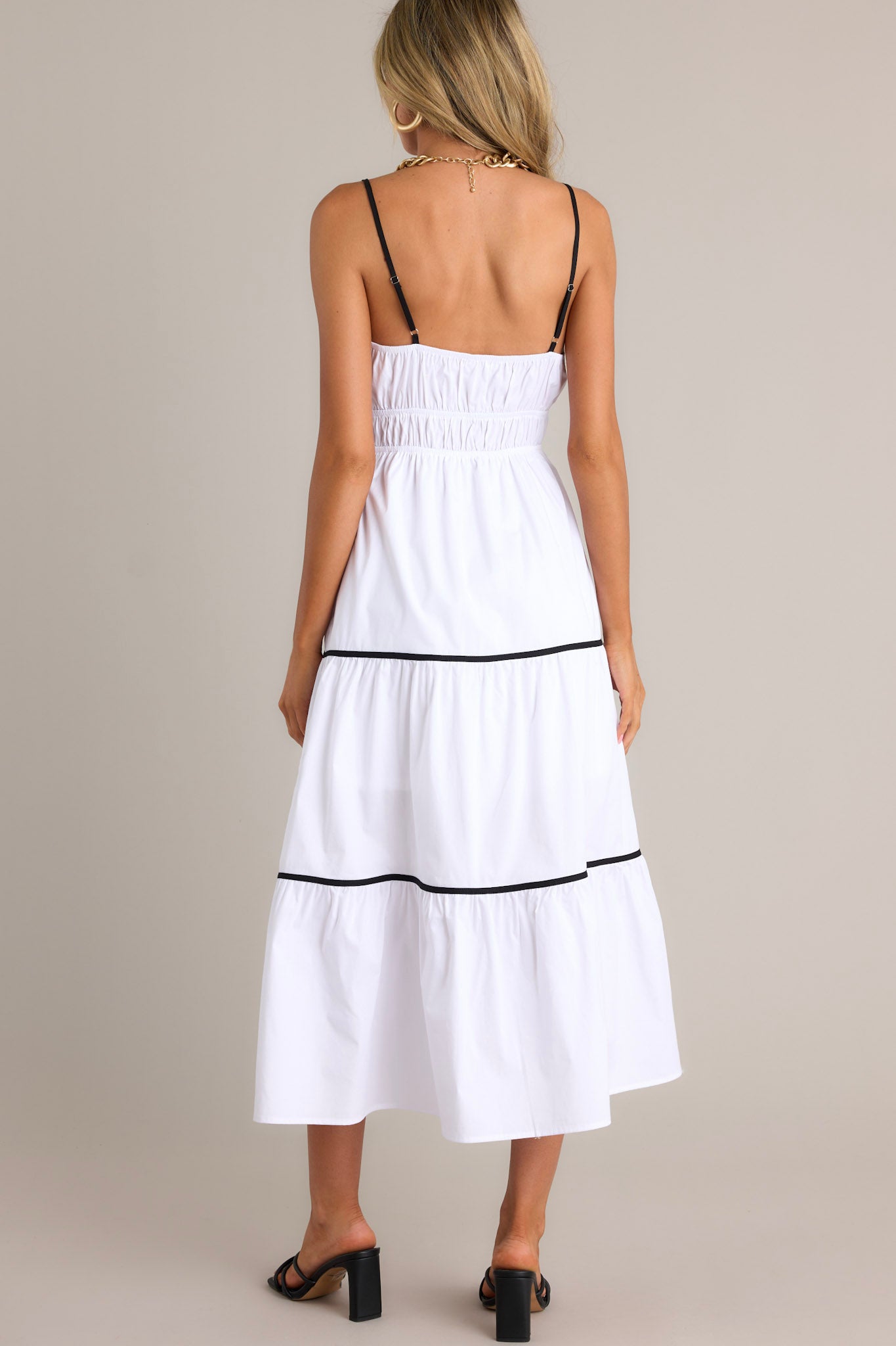 Back view of a white midi dress highlighting the thin adjustable straps, elastic waist, contrasting tiers, and overall fit.