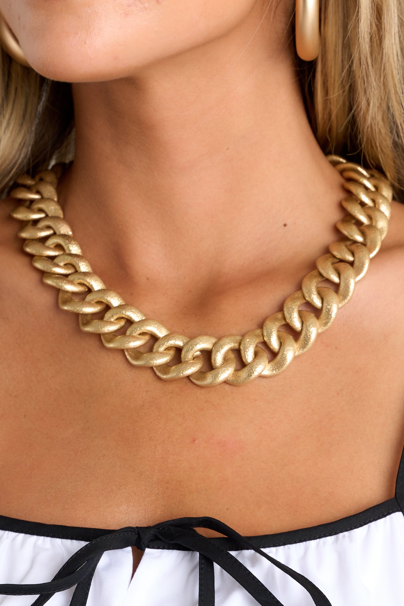 This gold necklace features a large curb chain design, a matte finish, a textured material, and a lobster claw closure.