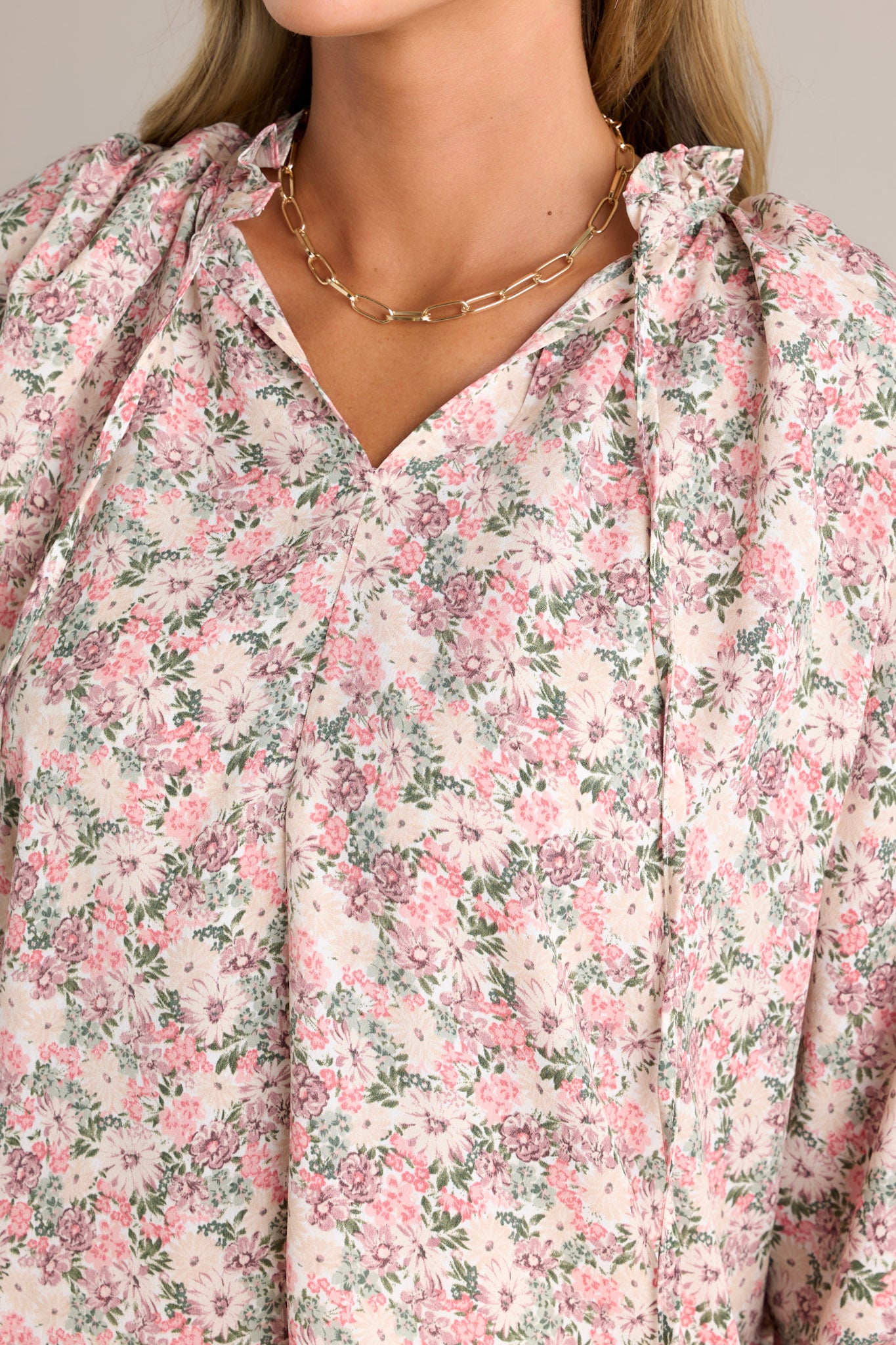 Close-up of the pink floral top showing the ruffled v-neckline, self-tie neck feature, and floral pattern.