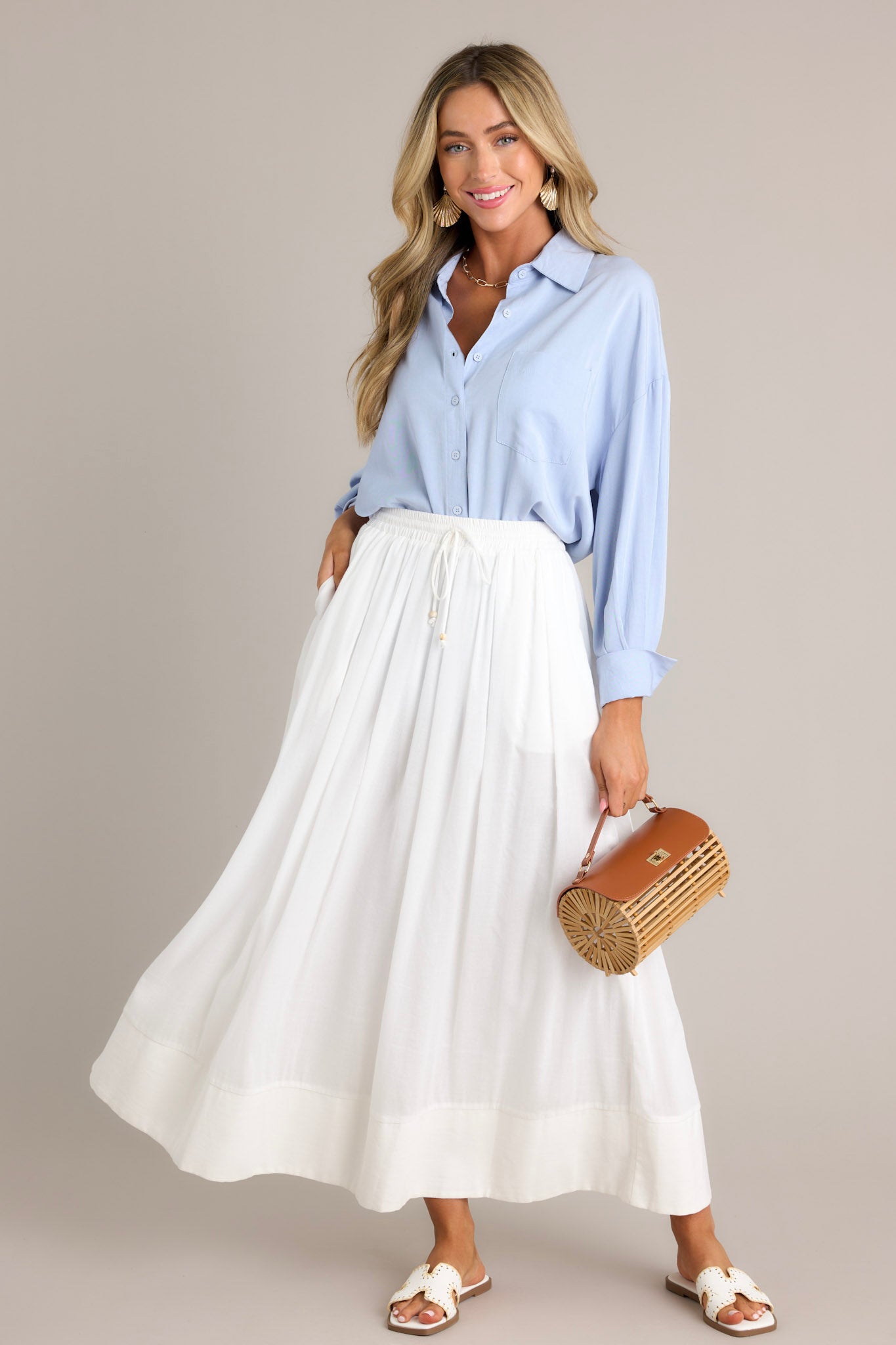 This white skirt features a high waisted design, an elastic waistband, a self-tie drawstring, functional pockets, flowing fabric, and a thick hemline.