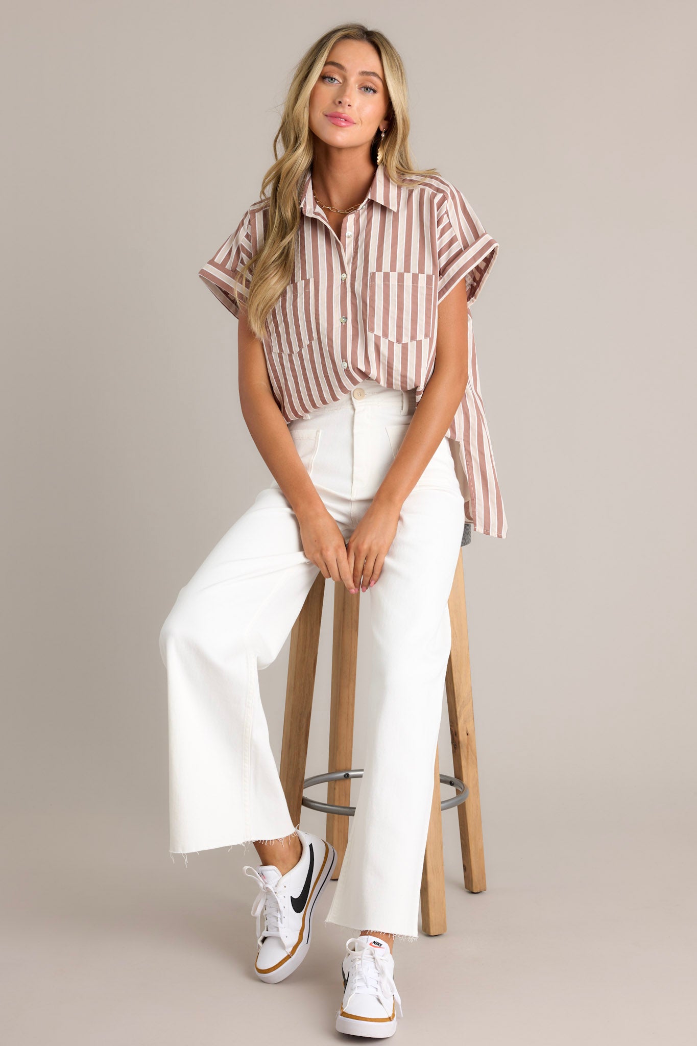 Front angled view of a tan stripe top featuring a collared neckline, a full button front, functional breast pockets, a vertical stripe design, cuffed short sleeves, and a split scooped hemline