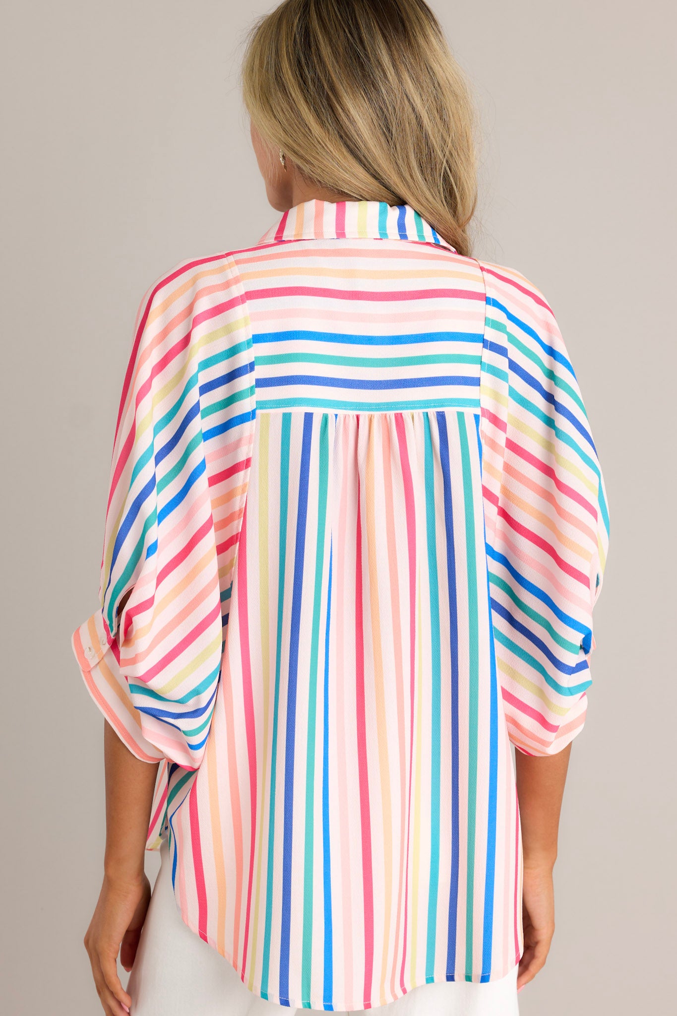 Back view of a rainbow stripe top highlighting the overall fit and wide dolman button cuffed sleeves.