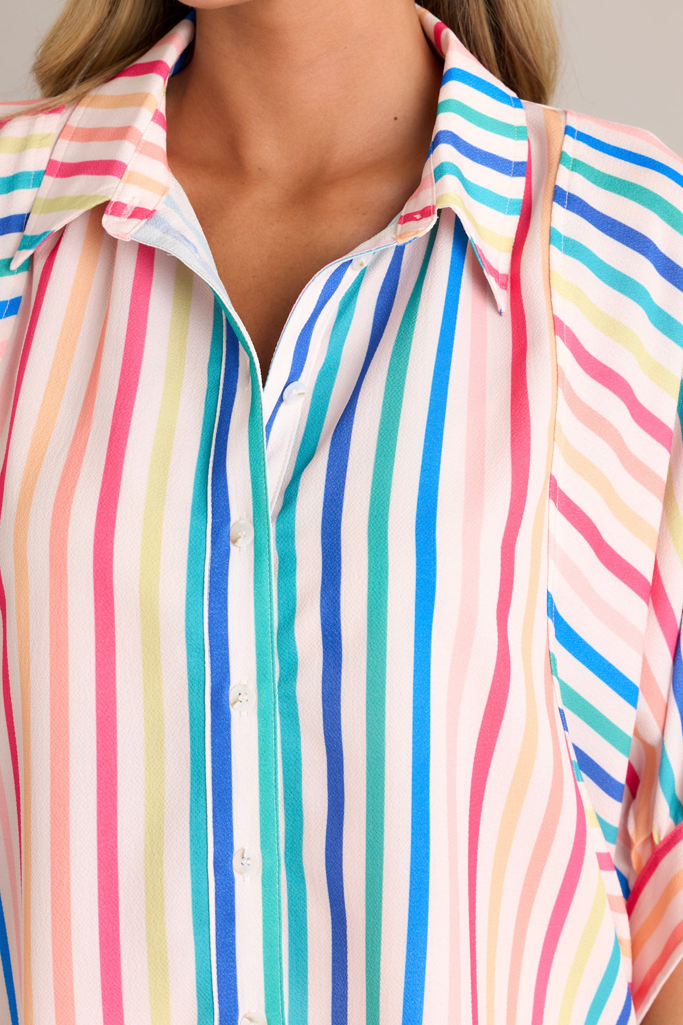 Close-up of the rainbow stripe top showing the collared neckline, full button front, and wide dolman button cuffed sleeves.