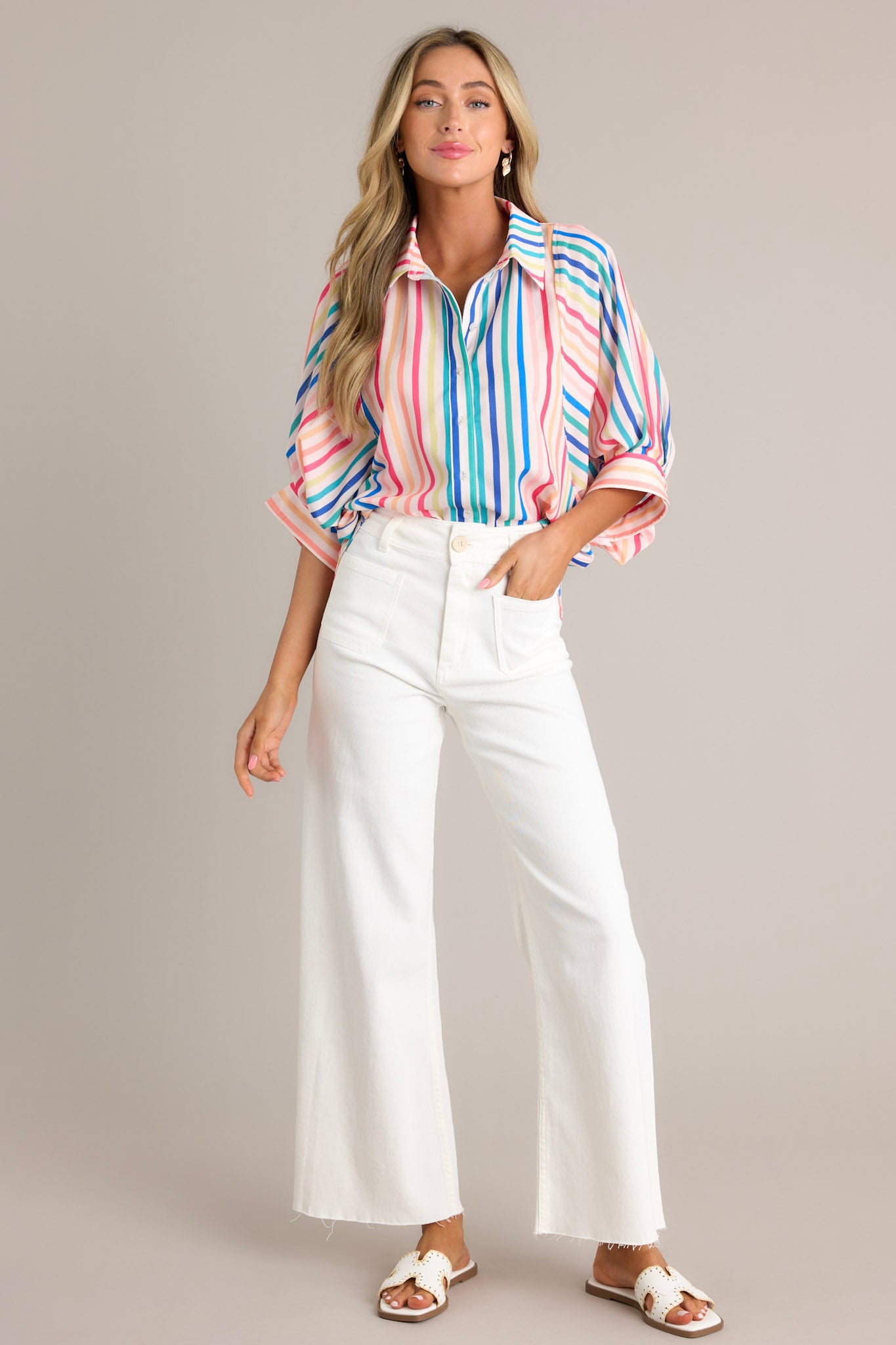 Full length view of a rainbow stripe top with a collared neckline, a full button front, an oversized fit, and wide dolman button cuffed sleeves