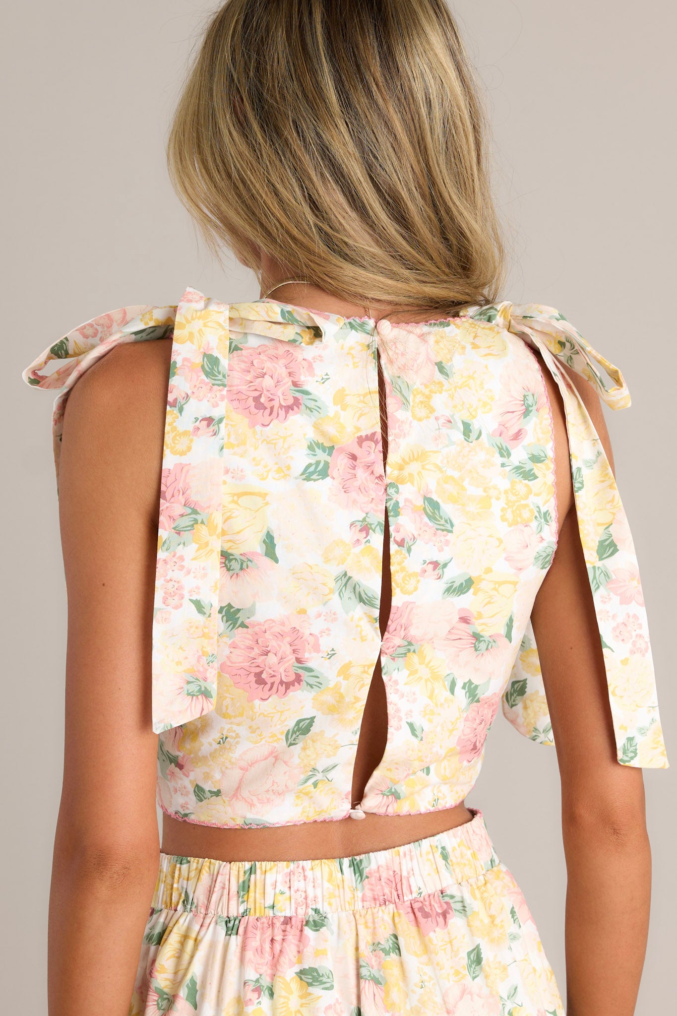 Back view of an ivory crop top highlighting the 3 functional buttons down the back, self-tie shoulder features, and cutouts.