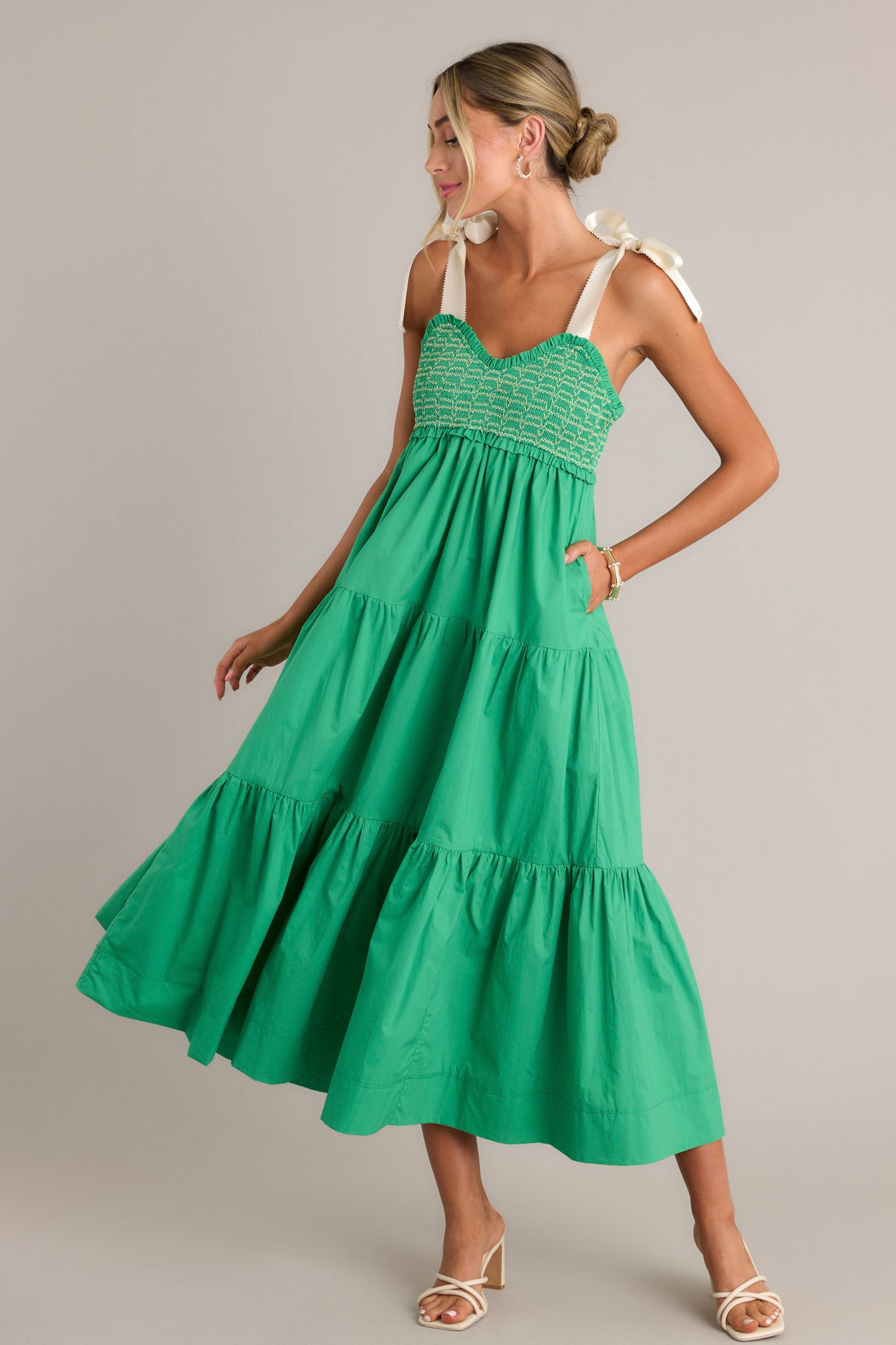 Action shot of a green maxi dress displaying the fit and movement, highlighting the v-neckline, thick self-tie straps, smocked bodice, functional hip pockets, and tiered design.