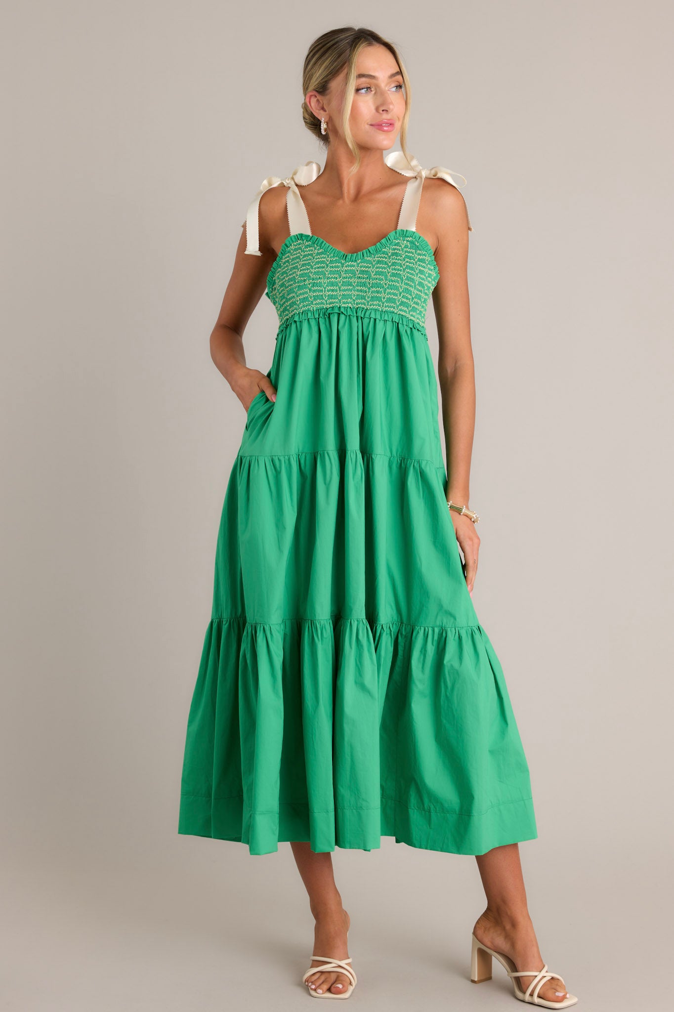 Full length view of a green maxi dress with a v-neckline, thick self-tie straps, a fully smocked bodice, functional hip pockets, and a tiered design