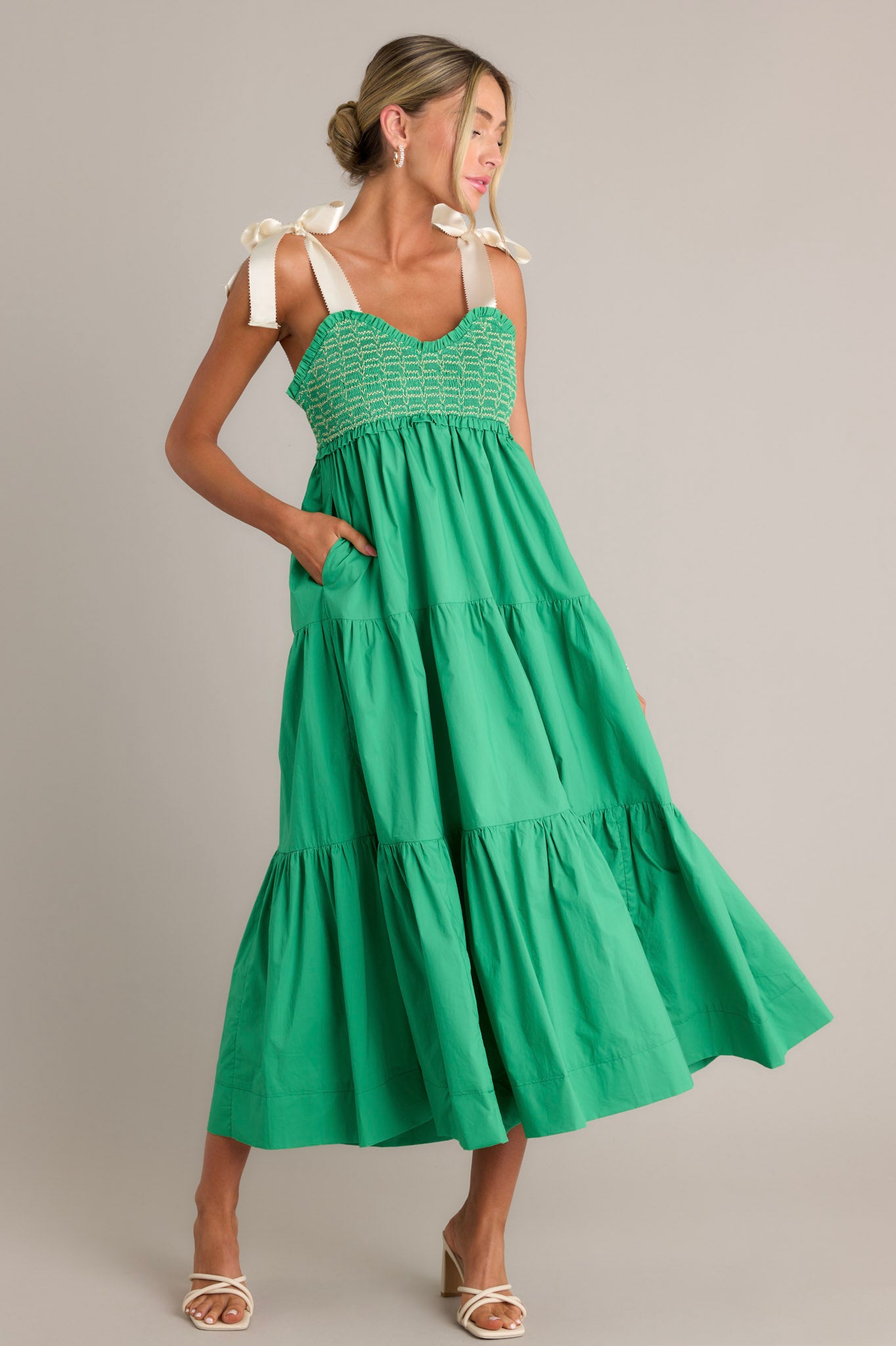 Front angled view of a green maxi dress featuring a v-neckline, thick self-tie straps, a fully smocked bodice, functional hip pockets, and a tiered design