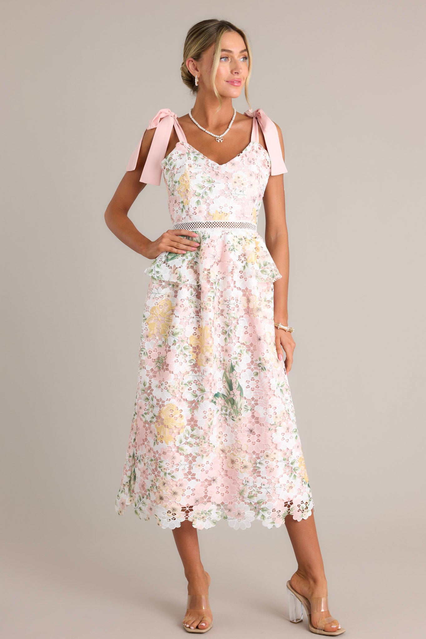 This white and pink dress features a v-neckline, self-tie straps, a zipper down the back, ruffle detailing at the waist, and a knitted lace overlay.