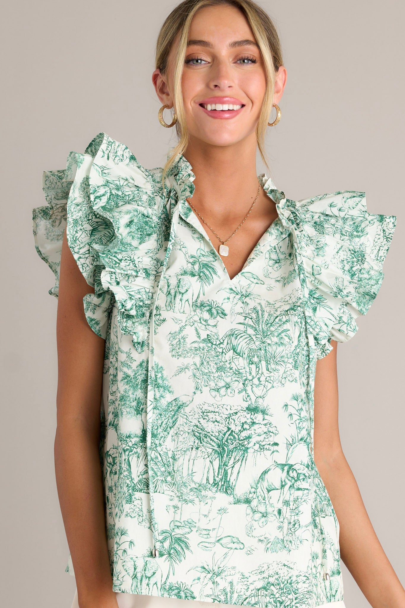 Front angled view of a green top featuring a ruffled v-neckline with a self-tie closure, a lightweight material, ruffle sleeves, and a toile print