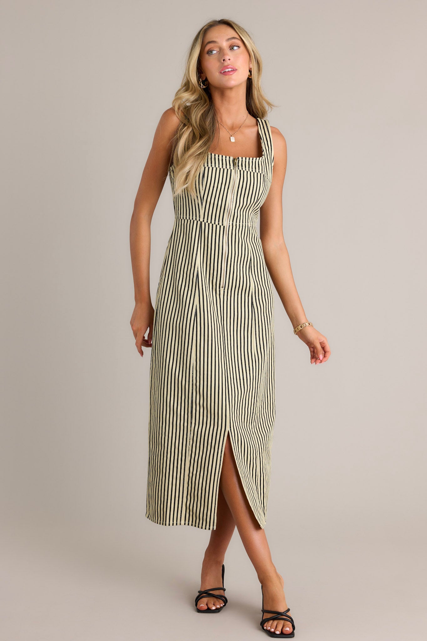 Full length view of a black stripe maxi dress with a square neckline, thick straps, a functional zip front, a vertical stripe pattern, and a front slit