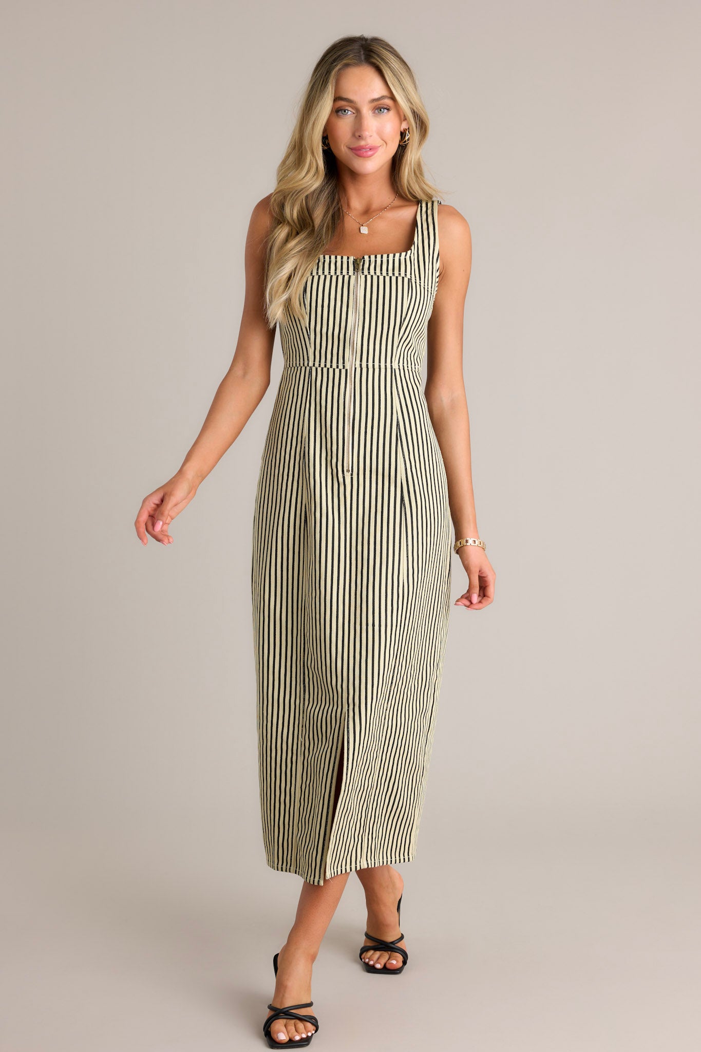 Front view of a black stripe maxi dress featuring a square neckline, thick straps, a functional zip front, a vertical stripe pattern, and a front slit.