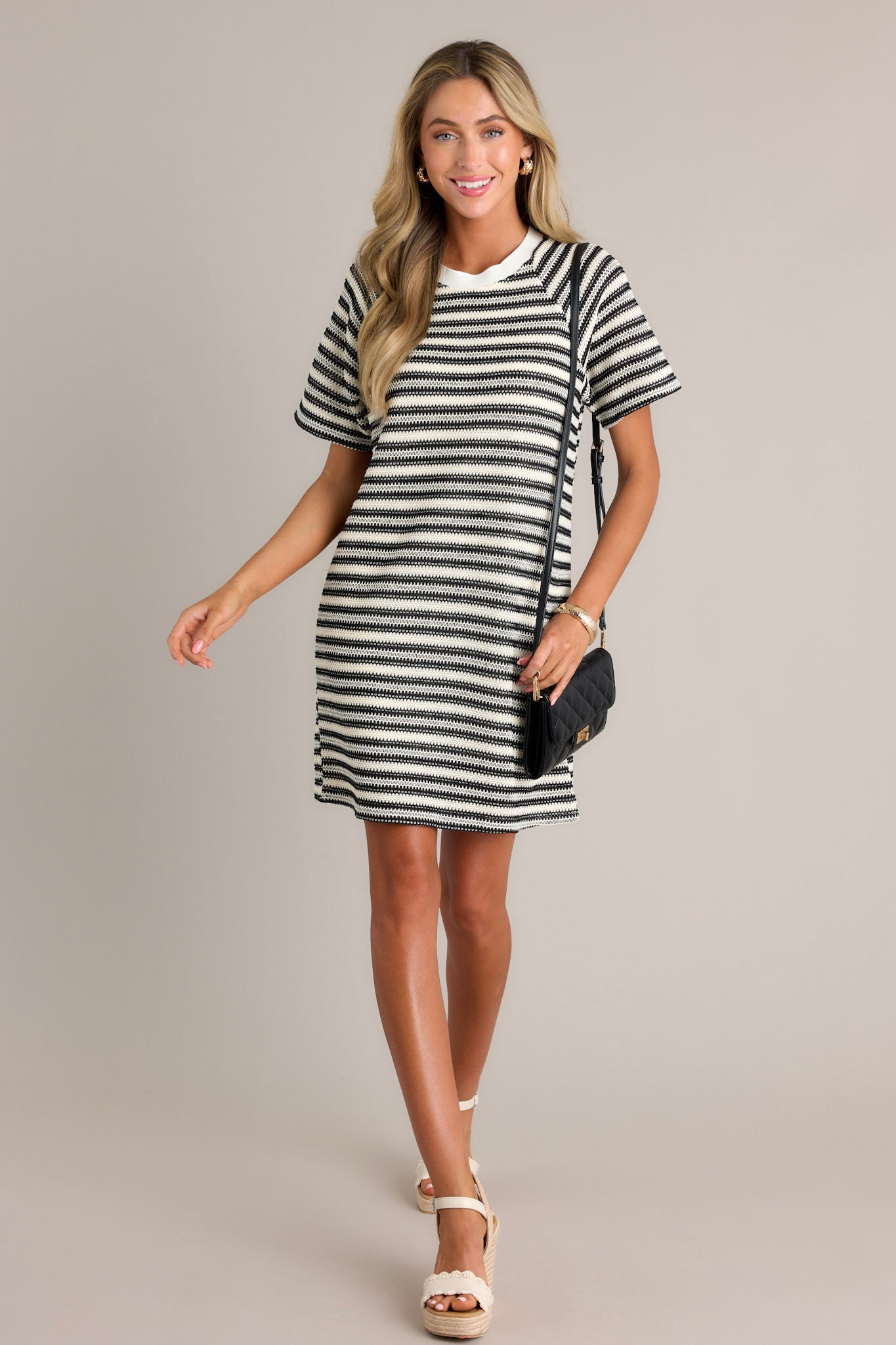 This black stripe mini dress features a crew neckline, a knitted horizontal stripe design, a relaxed fit, and short sleeves.