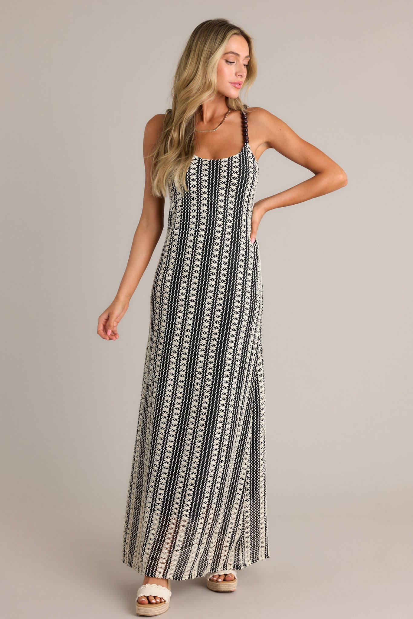 Action shot of a black stripe maxi dress displaying the fit and movement, highlighting the scoop neckline, fully beaded straps, knitted design, and vertical stripe pattern.