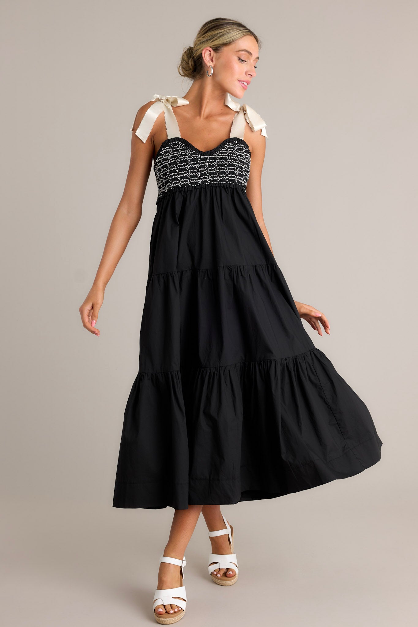 Full length view of a black maxi dress with a v-neckline, thick self-tie straps, a fully smocked bodice, functional hip pockets, and a tiered design