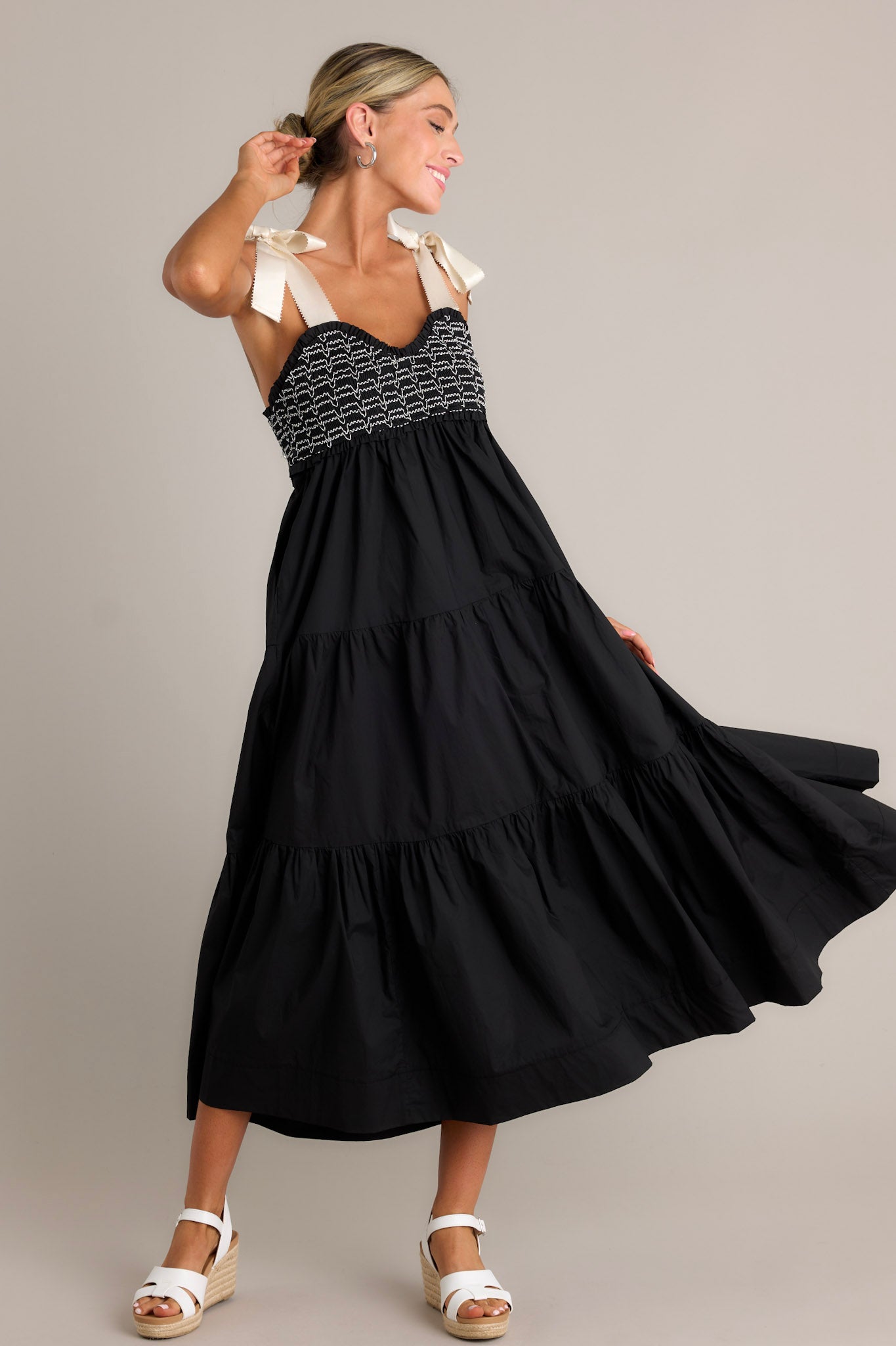Side view of a black maxi dress showcasing the v-neckline, thick self-tie straps, fully smocked bodice, functional hip pockets, and tiered design.
