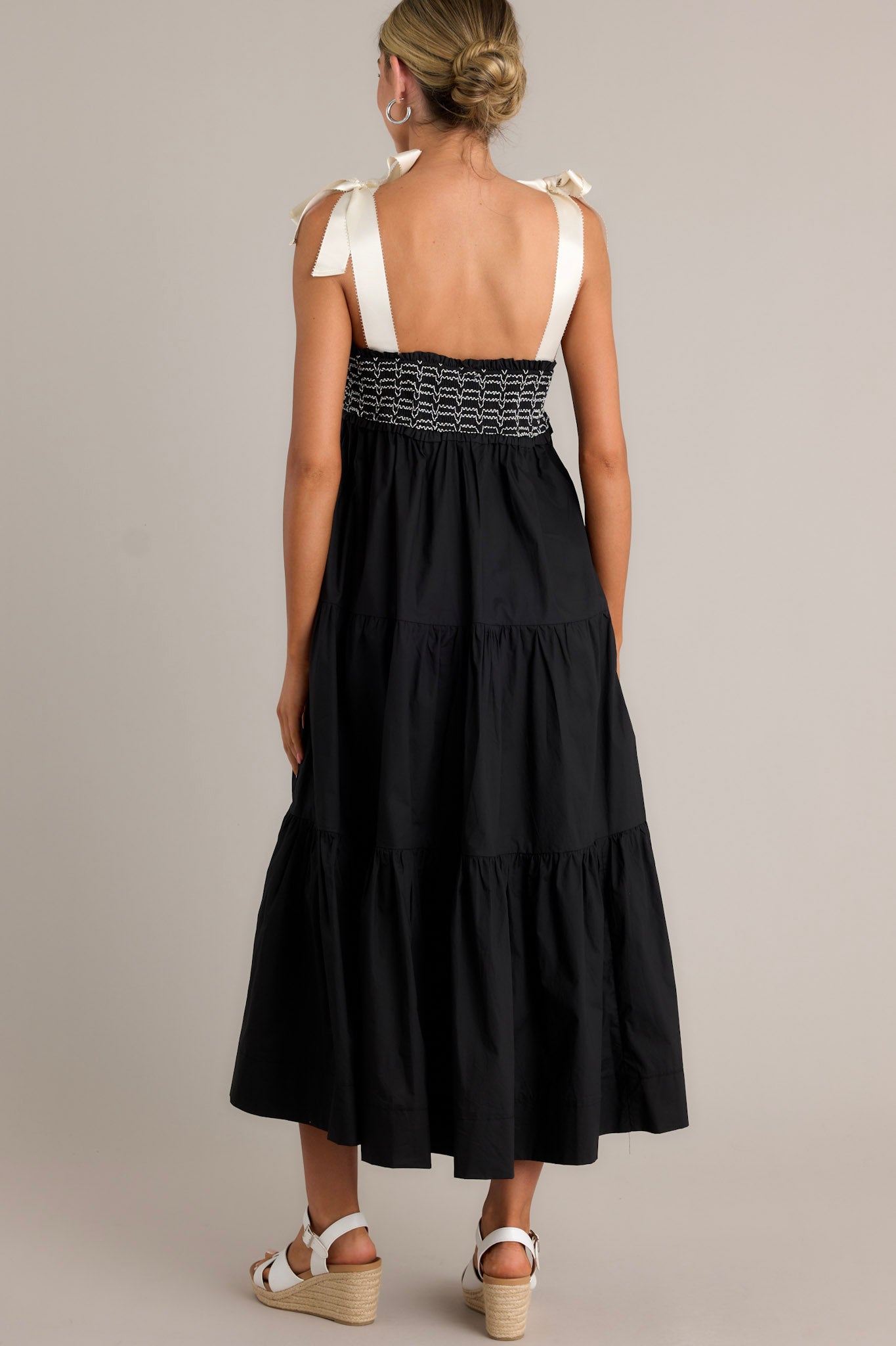 Back view of a black maxi dress highlighting the thick self-tie straps, fully smocked bodice, and overall fit.