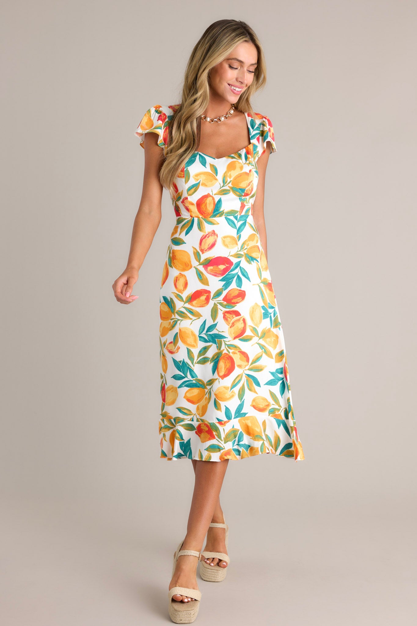 Action shot of an ivory dress displaying the fit and movement, highlighting the v-neckline, citrus print, ruffled hemline, and short flutter sleeves.