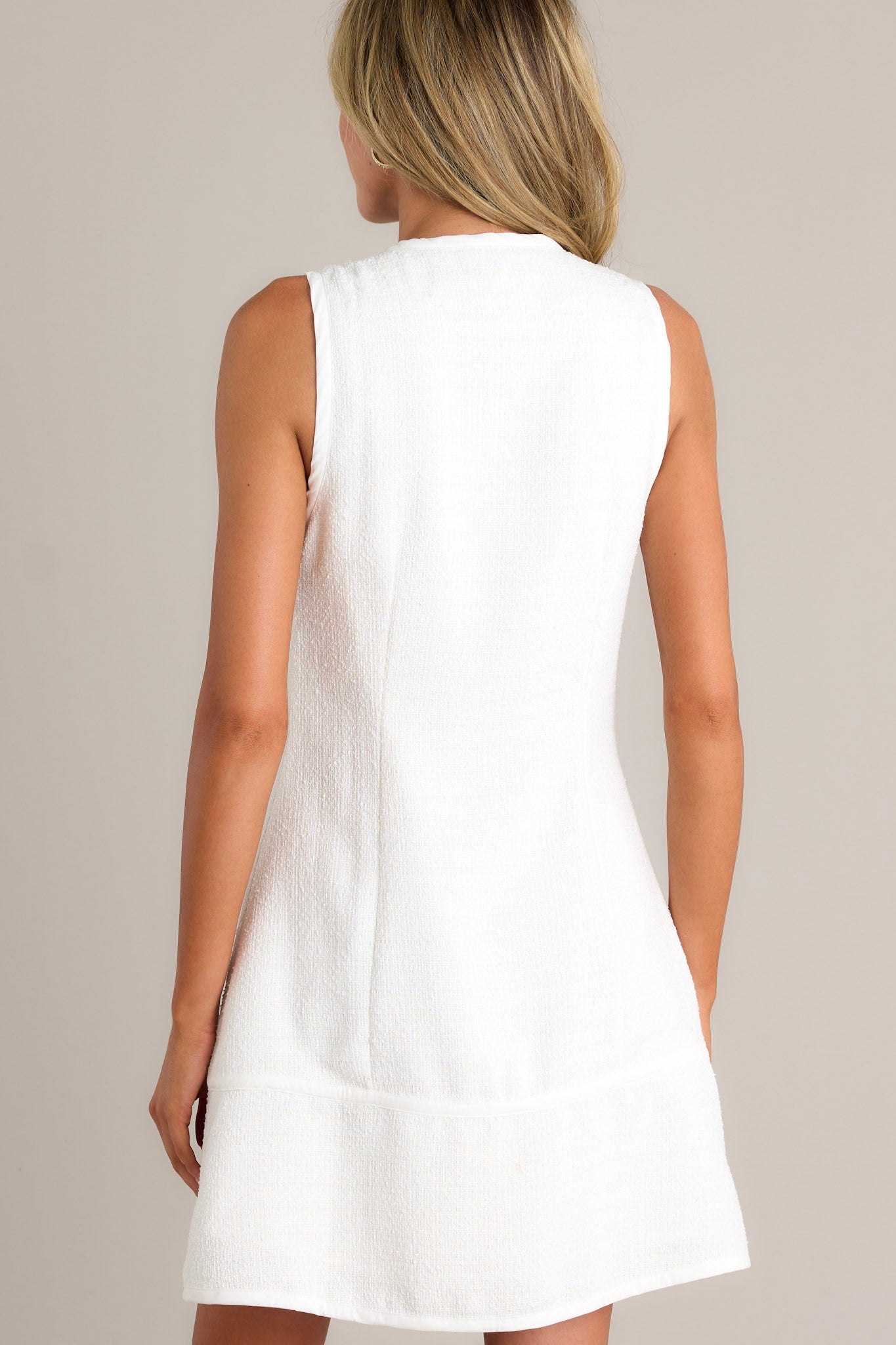 Back view of an ivory mini dress highlighting the high crew neckline, thick front seams, and overall fit.