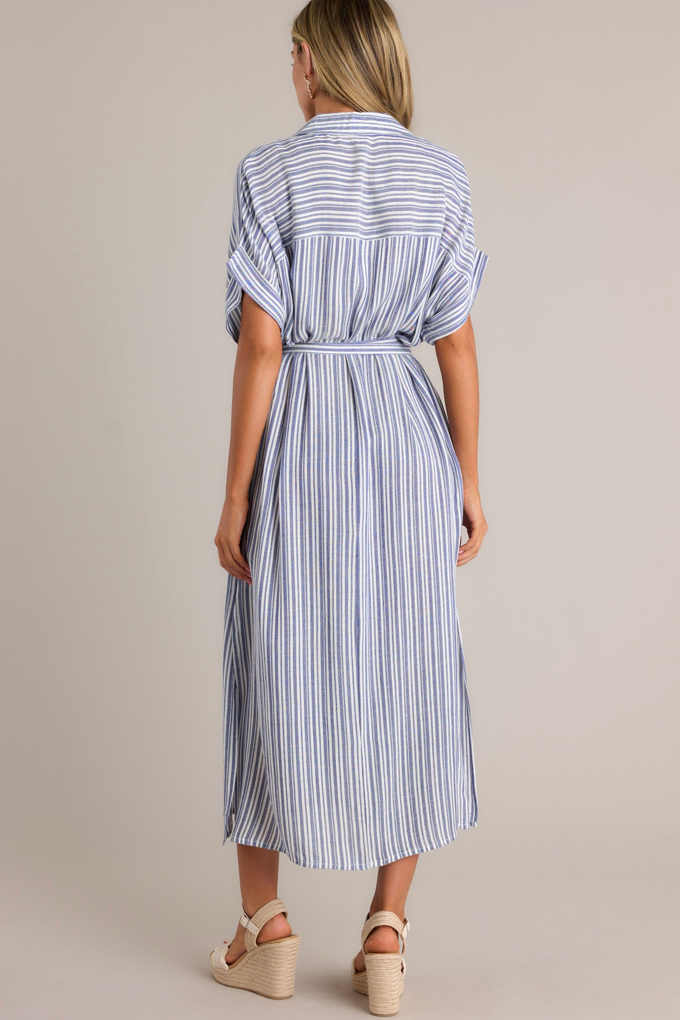 Back view of a blue stripe midi dress highlighting the overall fit, side slits, and flowing silhouette.