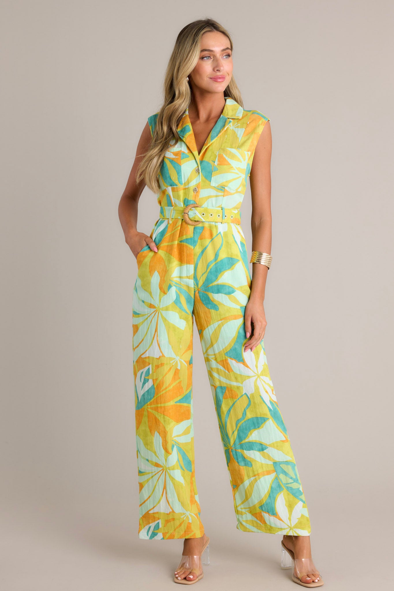 This lime green jumpsuit features a notched lapel collared v-neckline, breast pockets, functional buttons, an adjustable belt, belt loops, a functional zipper, functional hip pockets, and a wide leg design.