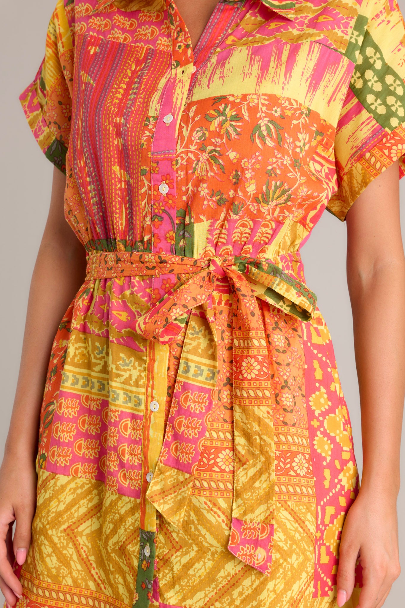 Close-up of the orange mini dress showing the collared neckline, full button front, and unique patchwork design.