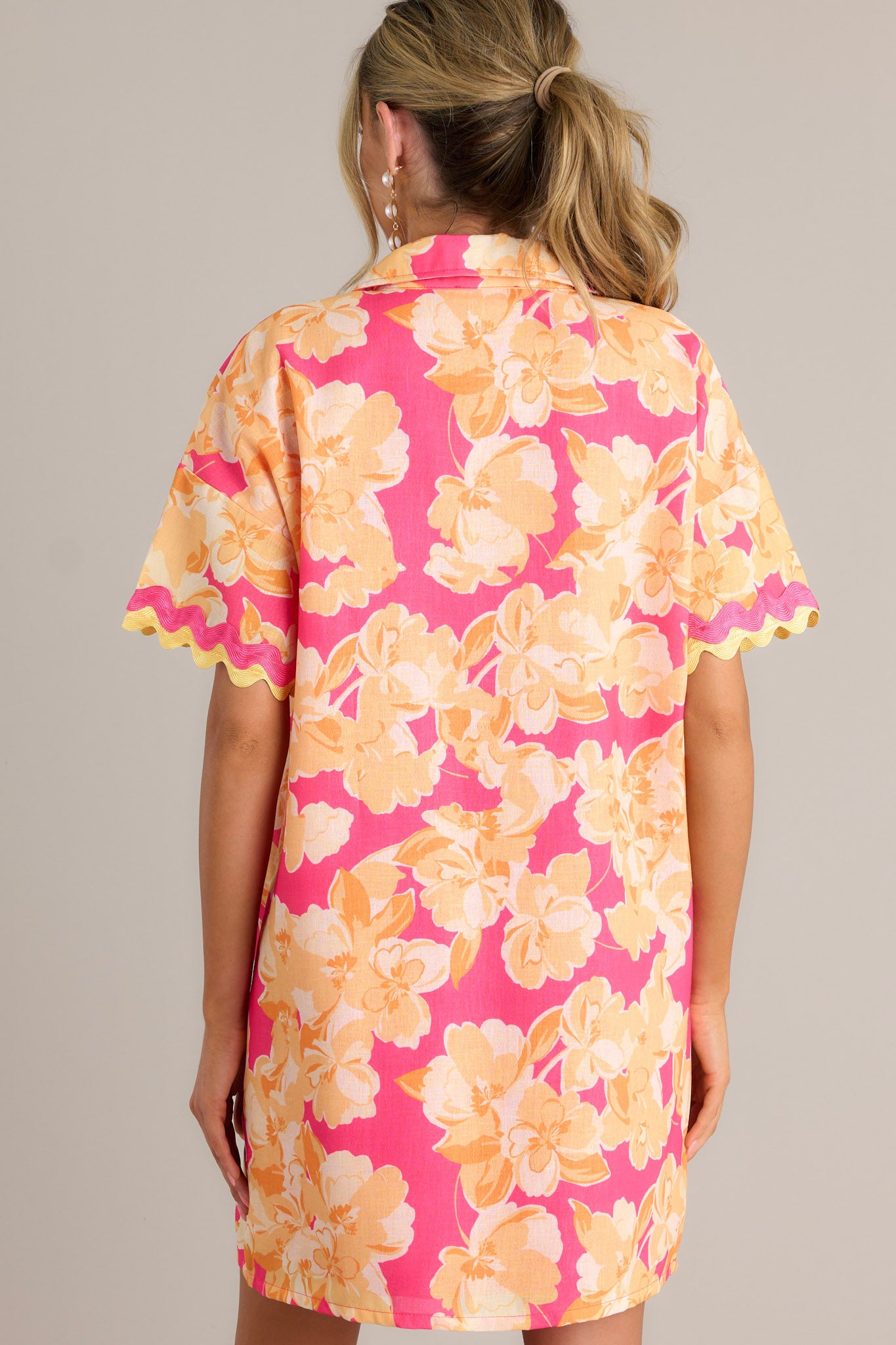 Back view of a pink floral mini dress highlighting the relaxed fit, short sleeves with ricrac trim, and overall design.