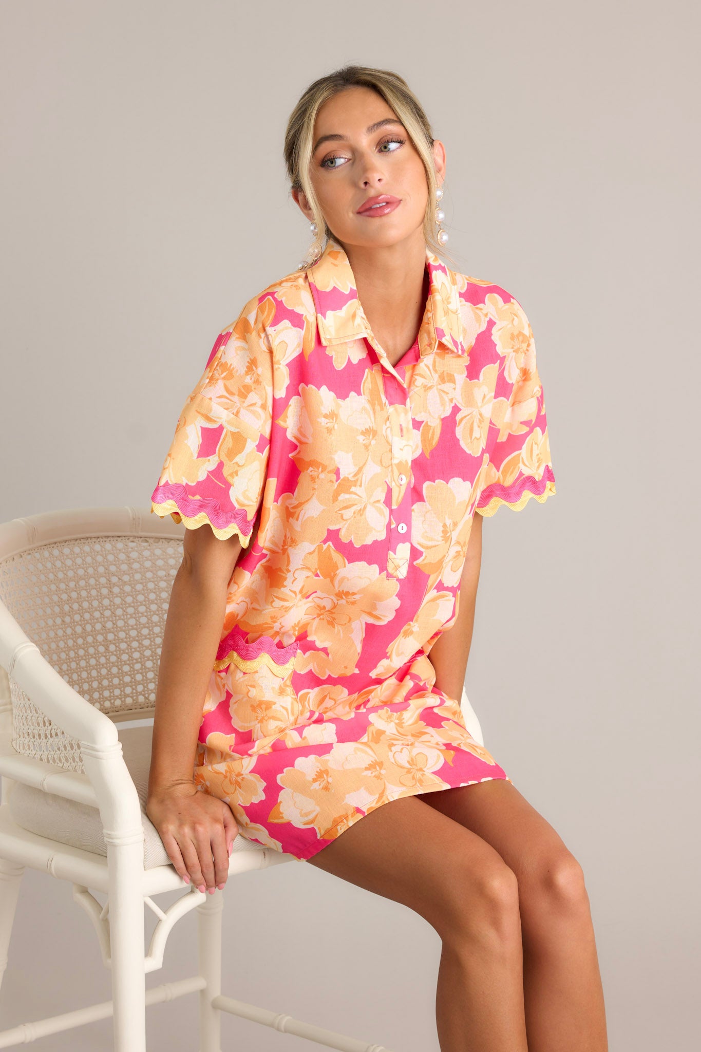 This pink floral mini dress features a collared neckline, a functional half button front, functional front pockets with ricrac detailing, short sleeves with ricrac trim, and a relaxed fit.